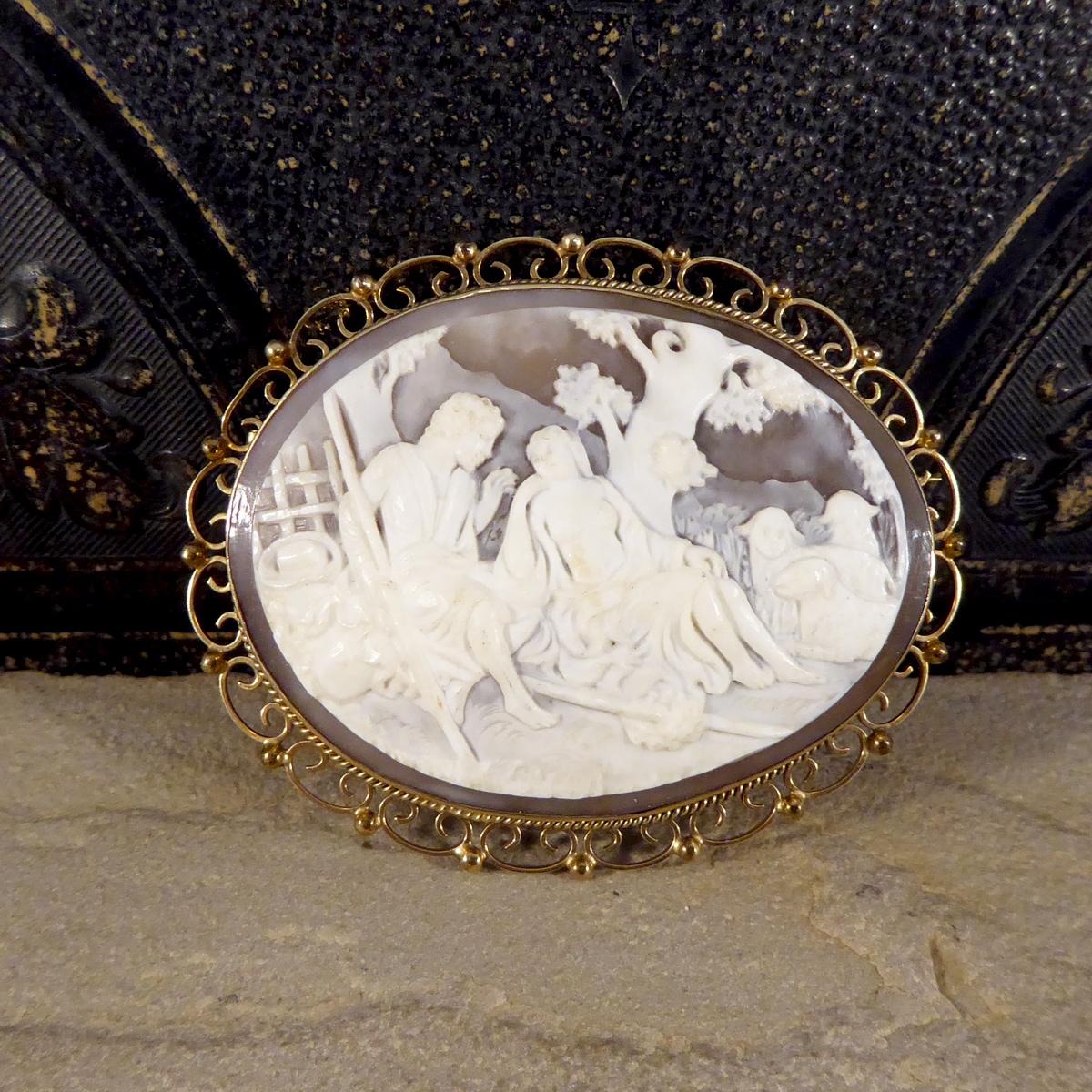 This brooch holds a large Cameo that has been carved to depict two people in an outdoor scene with sheep. It has been mounted in 9ct Yellow Gold with a decretive setting and border. With clear hallmarks on the side, this brooch has been hand crafted