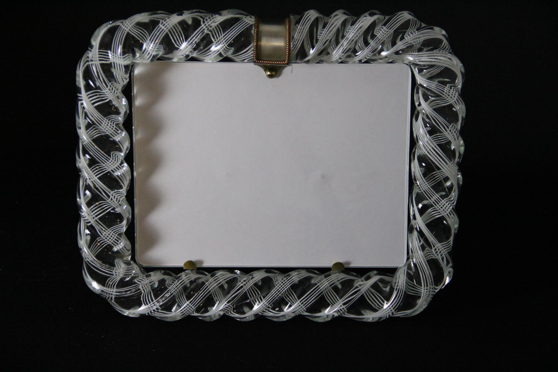 This beautiful horizontal photo frame is very rare. It is purely in the vénitien glass manufacturing  tradition. The technique used to get this rich optical effect is called filigrana and requires high skilled makers. 
This photo frame features