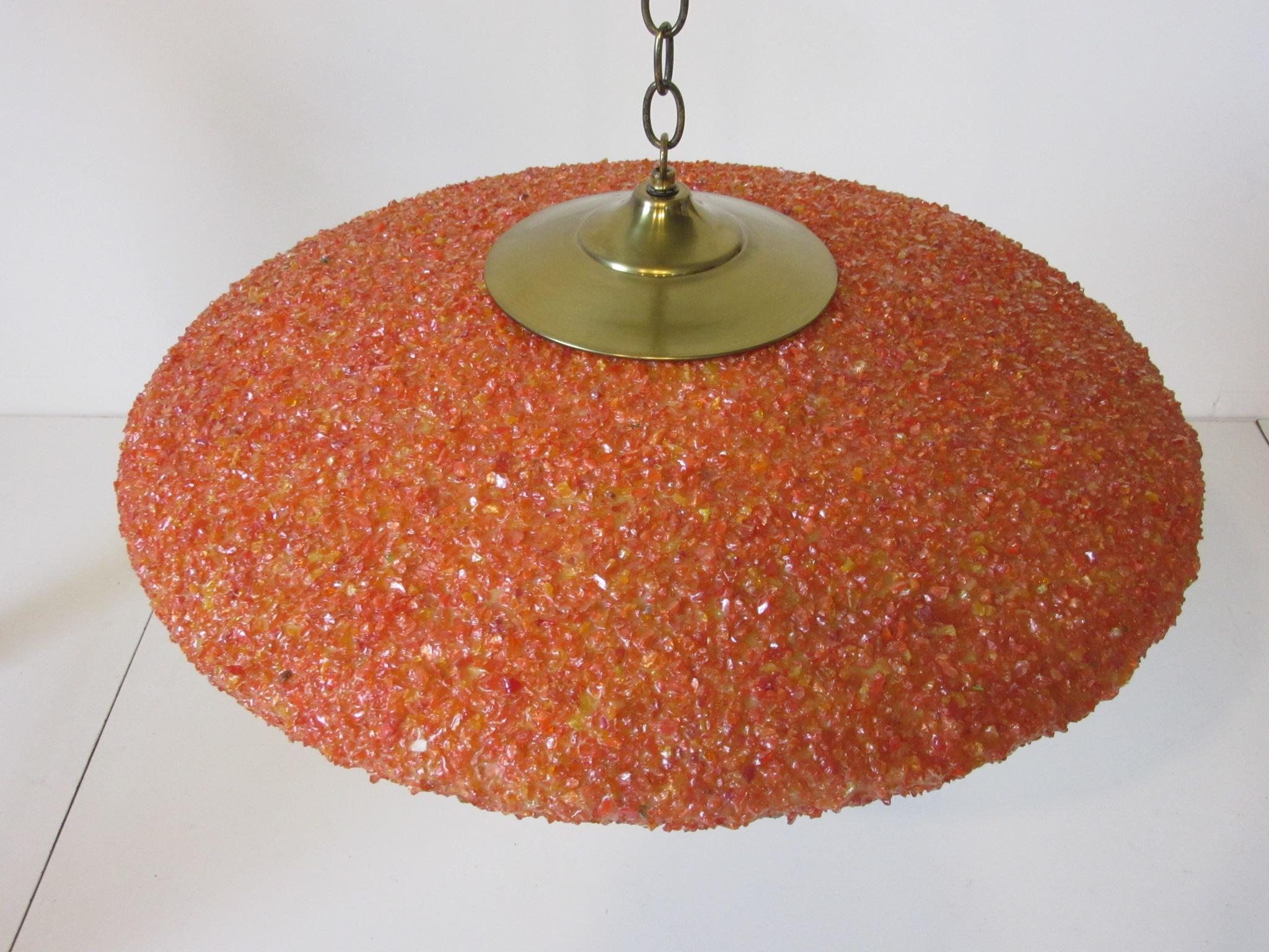 A large Nelson styled hanging flying saucer shaped ceiling light with orange and reddish toned small chunks of resin mounted to a fiberglass form with brass mounting plates and chain. Retains the manufactures tag from the Geringer Lighting Company.