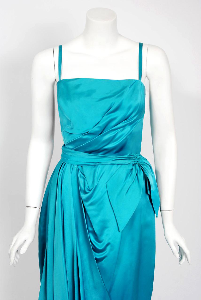 With its vivid aqua-blue color and flawless sculpted silhouette, this Lee Claire designer cocktail dress has the sophisticated elegance the 1950's were known for. The construction is clearly inspired by the draping techniques of Charles James or