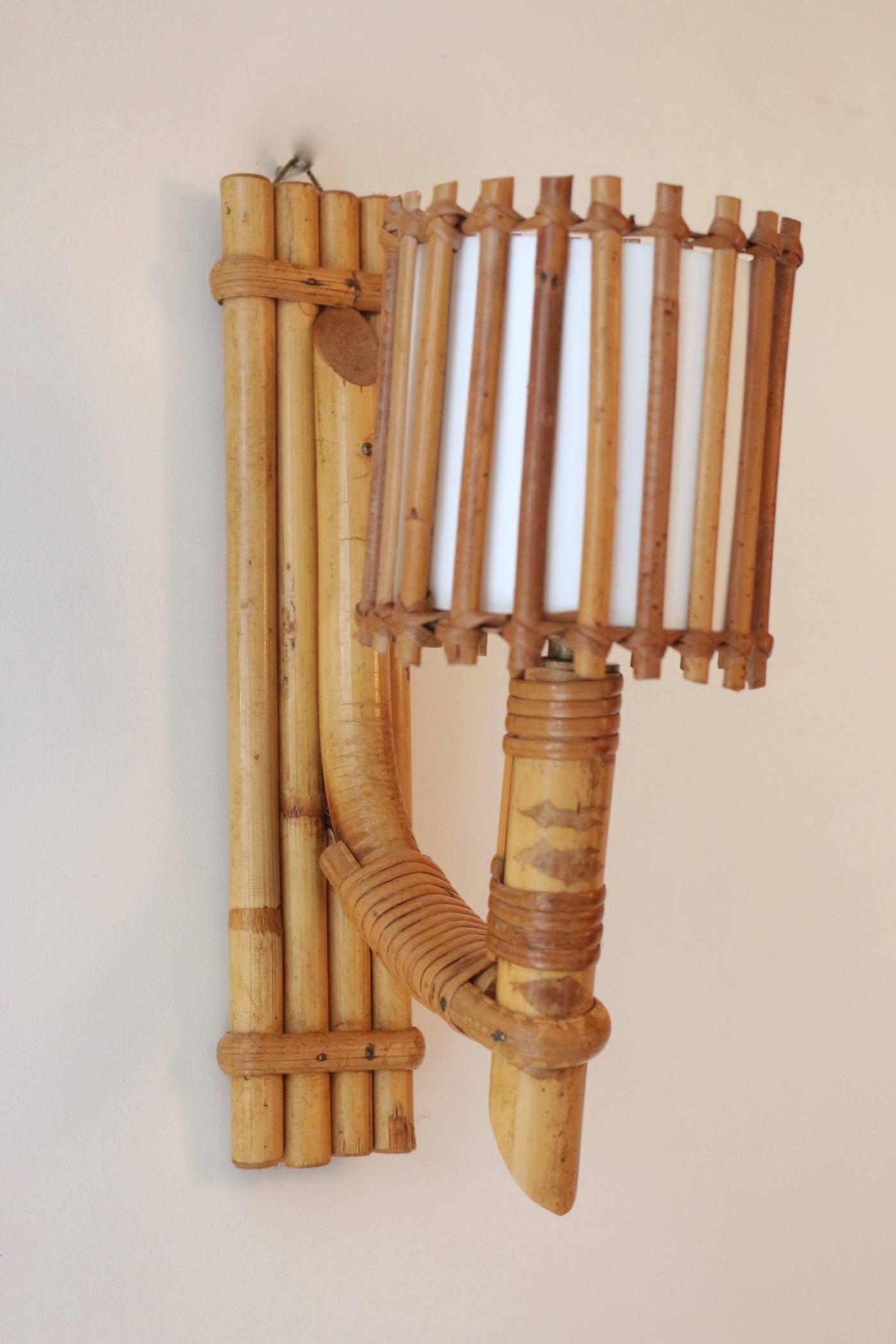 1950s, Louis Sognot pair of rattan sconces.

Composed of a wall support formed of several bamboo rods assembled vertically by bamboo wire ties
on which by an arm of light composed of a descending bamboo rod
on which is positioned another bamboo