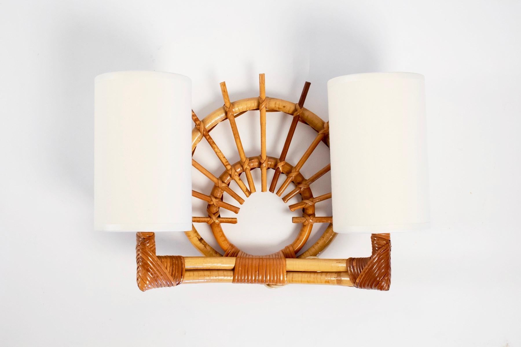 The back plate is a stylize sun composed with two concentric rattan ring.
Two lighted arms ended with two cylindrical white cotton shades.
2 bulbs per sconces.
 