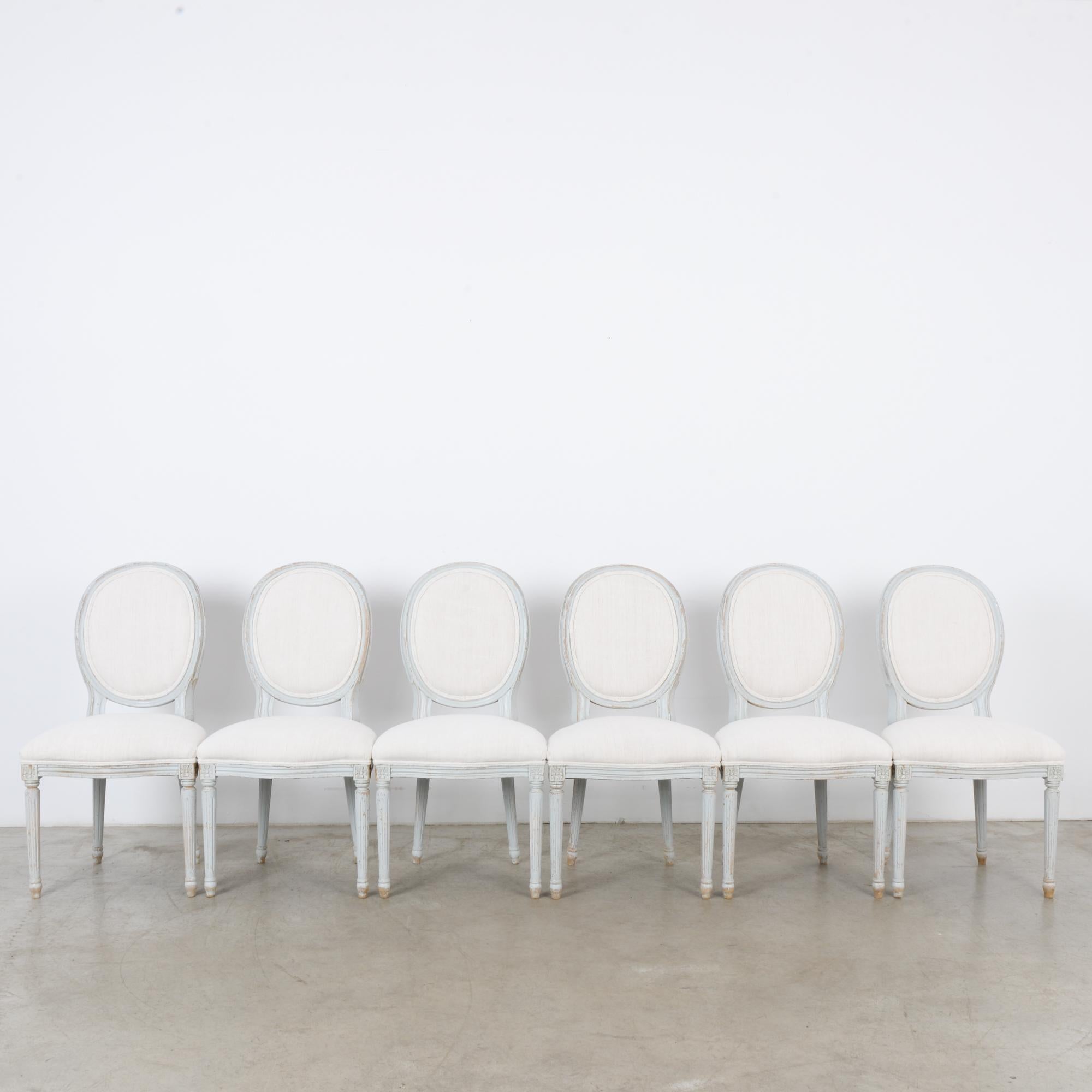 A set of six white wooden dining chairs from France, circa 1950. A Louis XVI Silhouette with a balloon back and a wide seat upon tapered, fluted legs. Carved accents add a decorative touch. The seat and chair-back have been reupholstered in a
