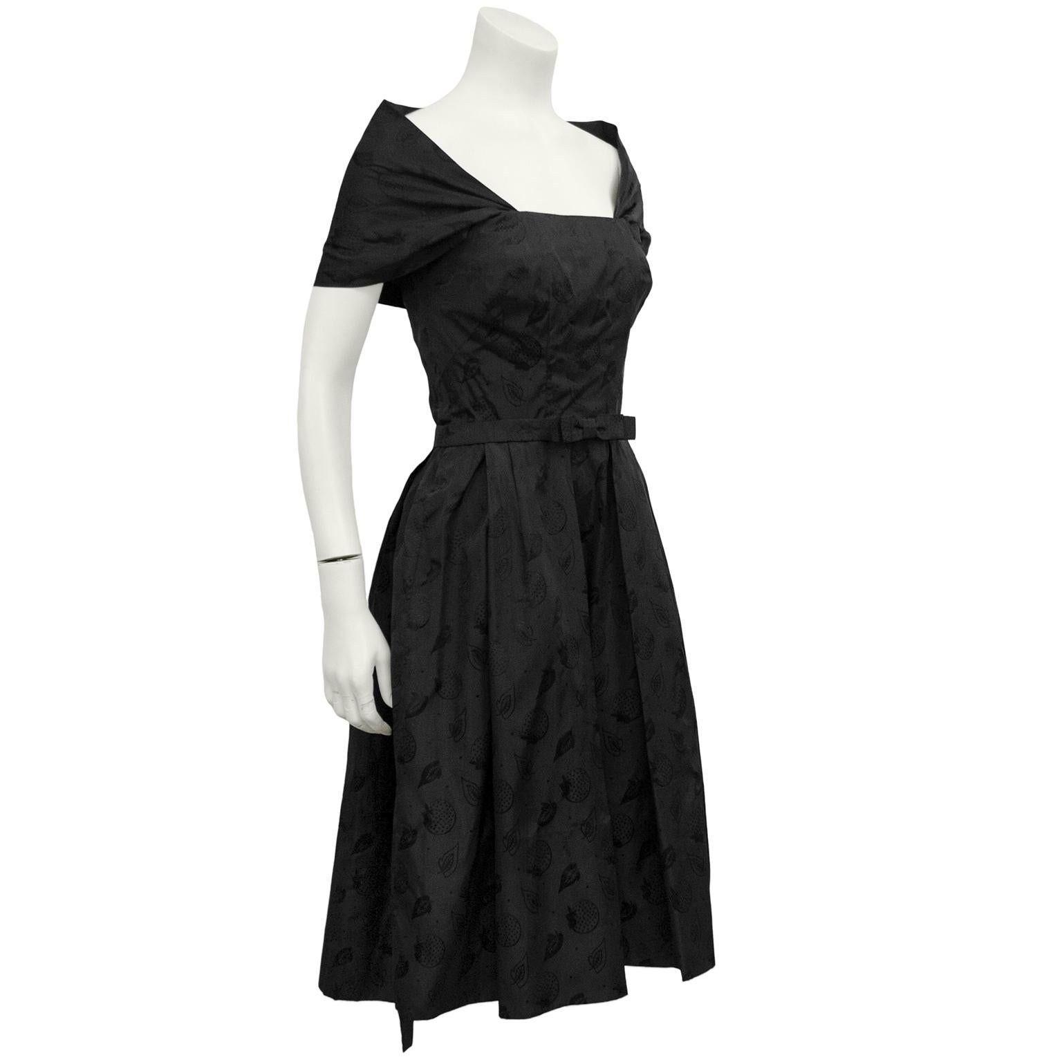 Stunning hard to find 1950s Mainbocher cocktail dress. Monochromatic black silk jacquard with an all over leaf and orange pattern. Stole style attached collar with fitted bodice, slim waist belt with flat bow detail and a full aline skirt with box