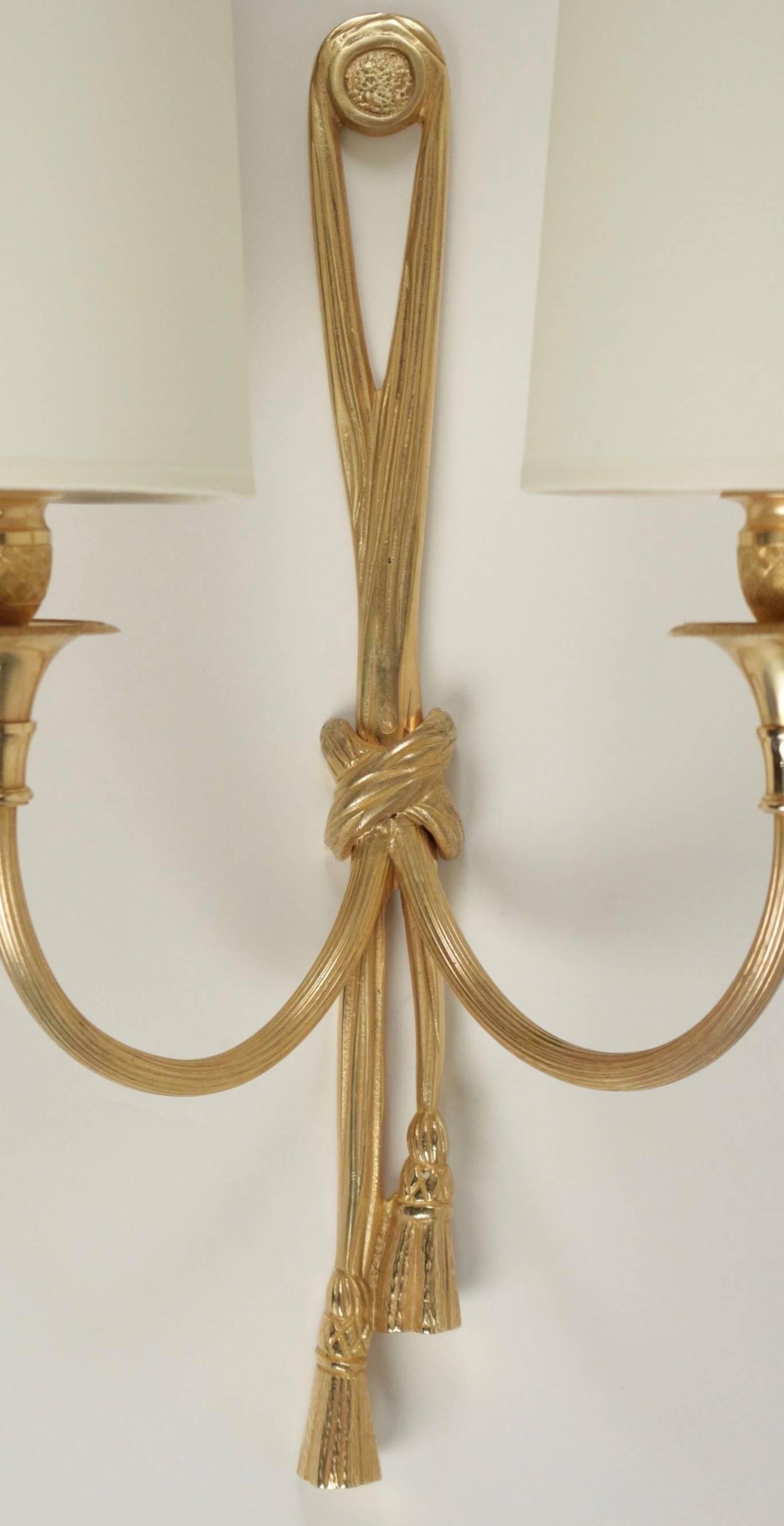 1950s Maison Baguès large pair of neoclassical sconces.

A ribbon with two pompoms made of bronze forms the back plate.
Two lighted arms made of brass. Handmade lampshades made of with ivory cotton.

Two bulbs per sconce.
 