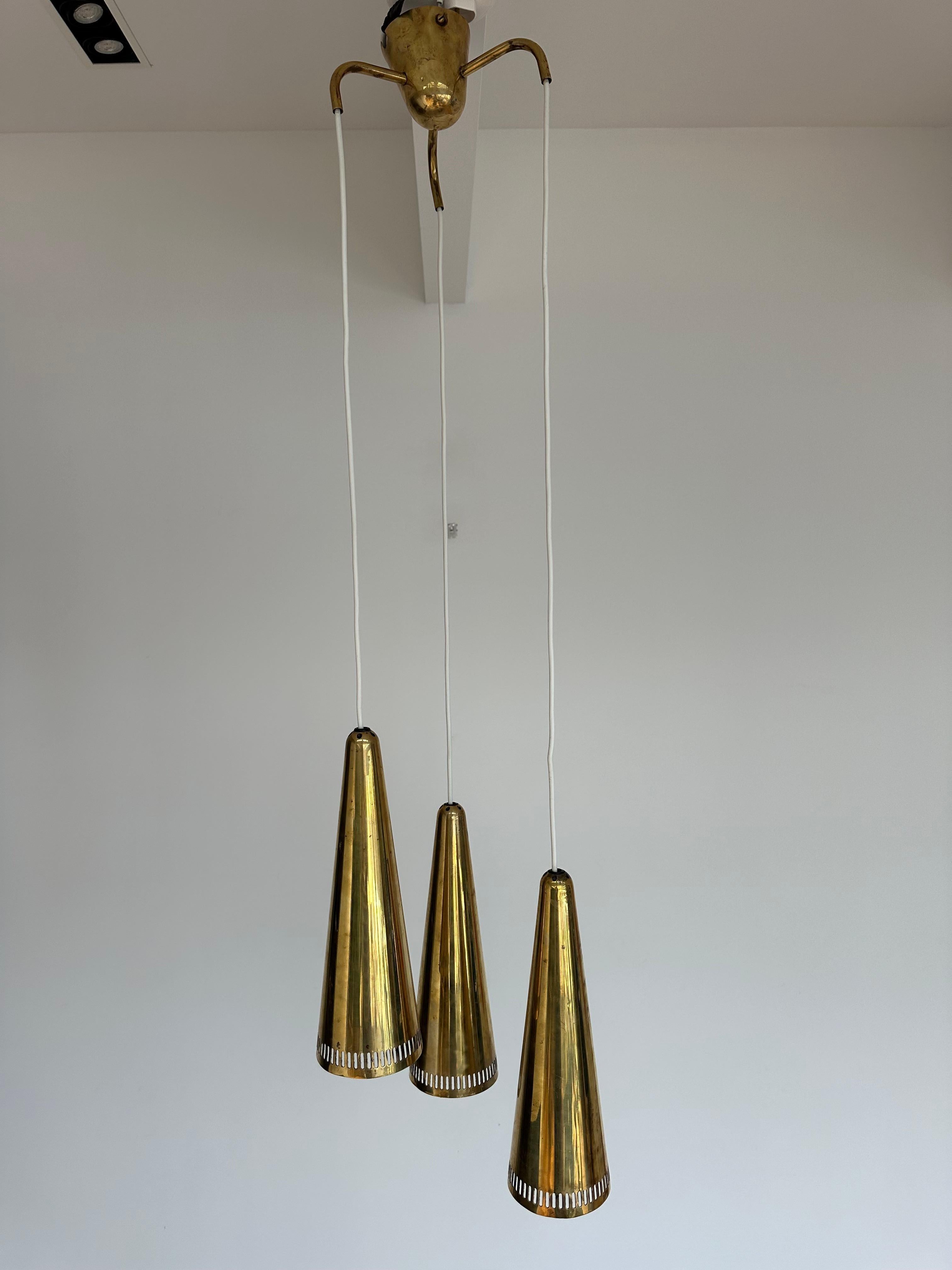 1950s Mauri Almari 'K2-48' brass chandelier for Idman. A rare example, this cascading chandelier features a trio of perforated brass cones that each measure 33cm H x 11 cm W with the original brass canopy. Highly reminiscent of Paavo Tynell's iconic