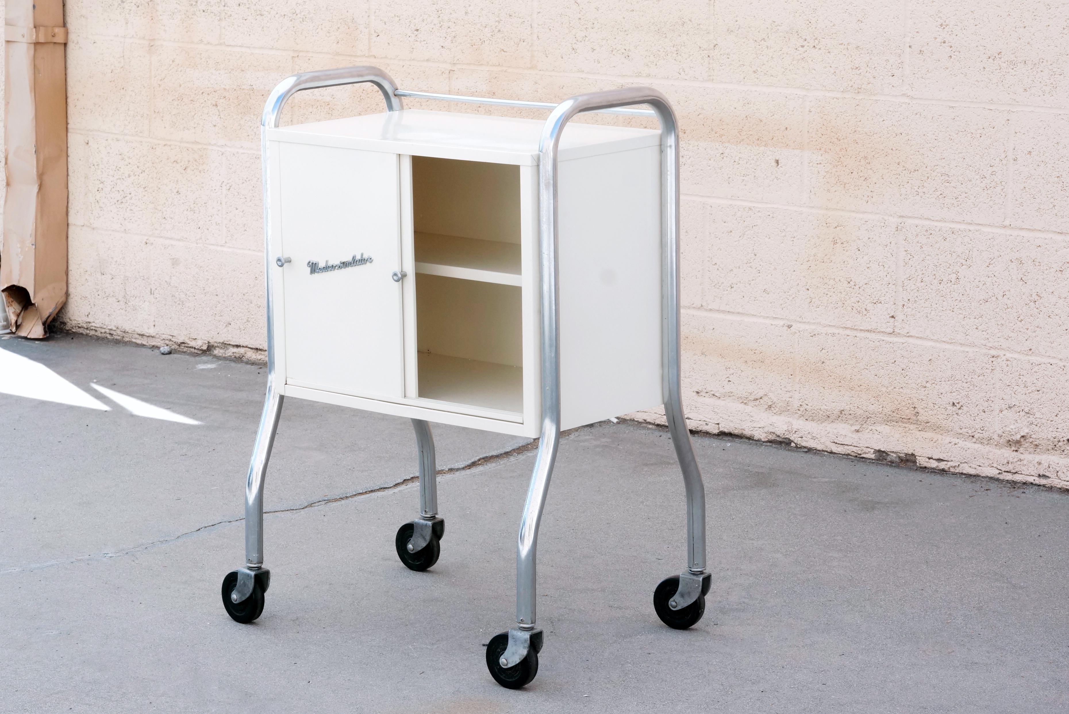 Super retro medcosonlator rolling medical cabinet. With tubular chrome frame, sliding doors, and iconic logo and original cream paint. Could make for a great little bar cart or office piece. Chrome is in original condition and shows light wear;