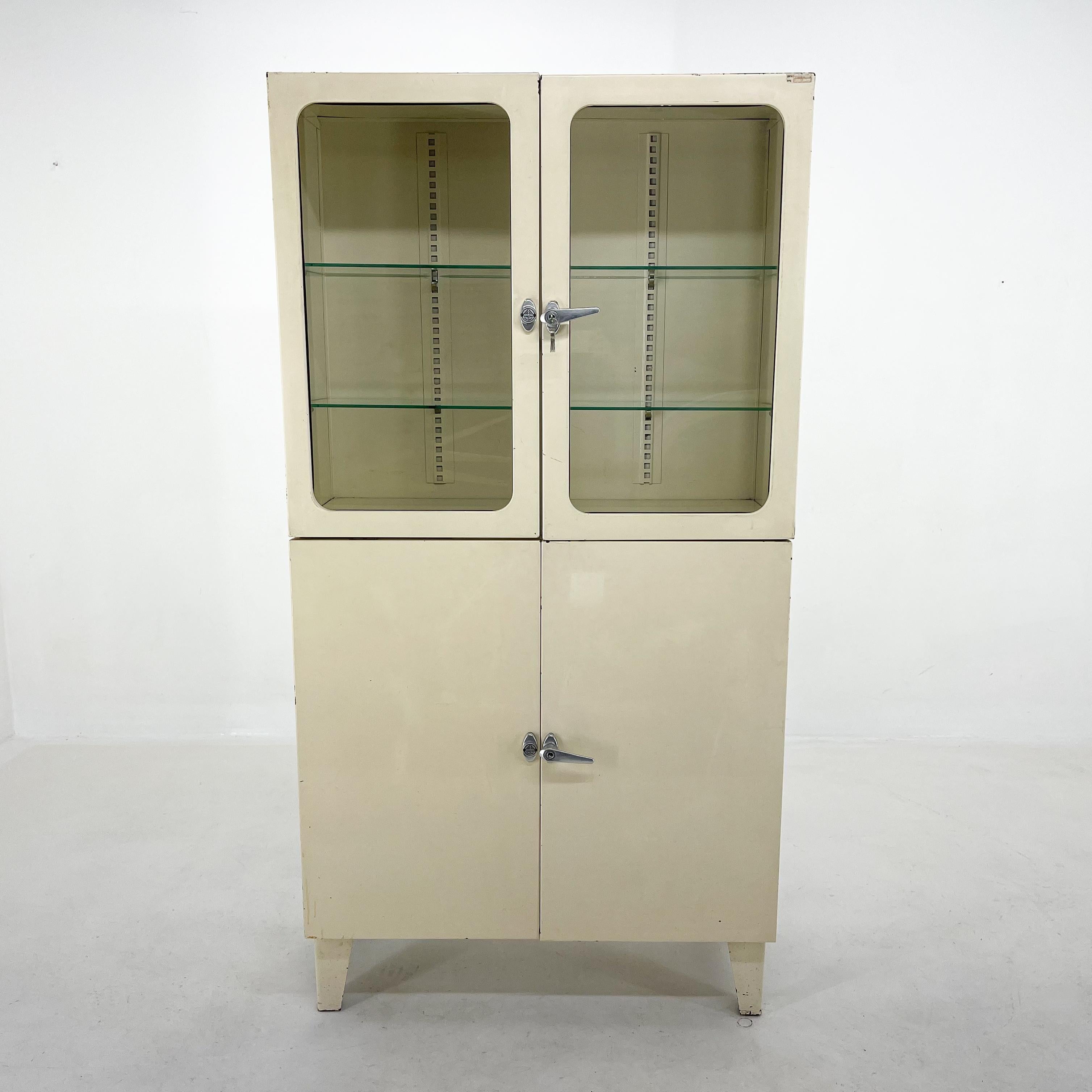 Vintage metal cabinet with two separate sections and glass shelves. Made by Smrecina OZ Pukavec in the former Czechoslovakia in the 1950's. The cabinet's doors are fully functional with original set of keys.