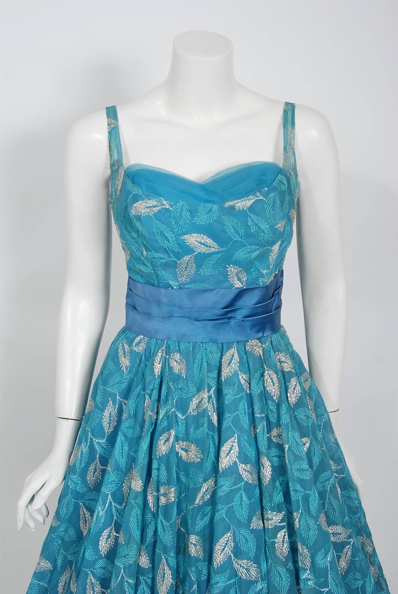 Fashioned from metallic leaf-motif embroidered teal blue chiffon, this 1950's Will Steinman creation has everything a woman wants. The bodice has a gorgeous sweetheart tulle-trimmed plunge. I adore the hourglass cummerbund sash waist which flows