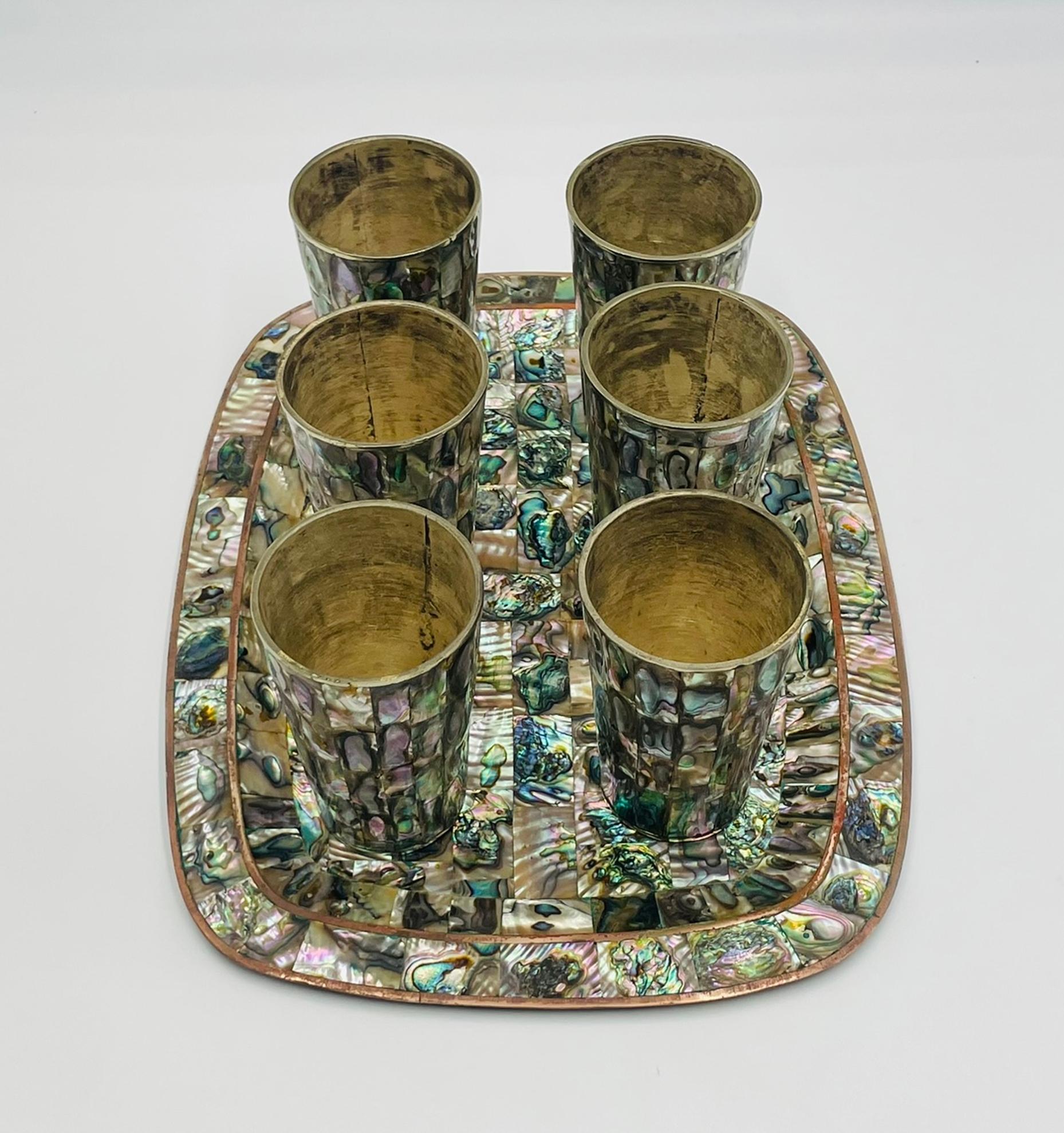 Elegant mid-century Mexican brass and abalone shell serving set, designed and handcrafted in Mexico during the 1950s. This beautiful ensemble includes a rectangular tray and five tumblers, each intricately inlaid with iridescent abalone shell