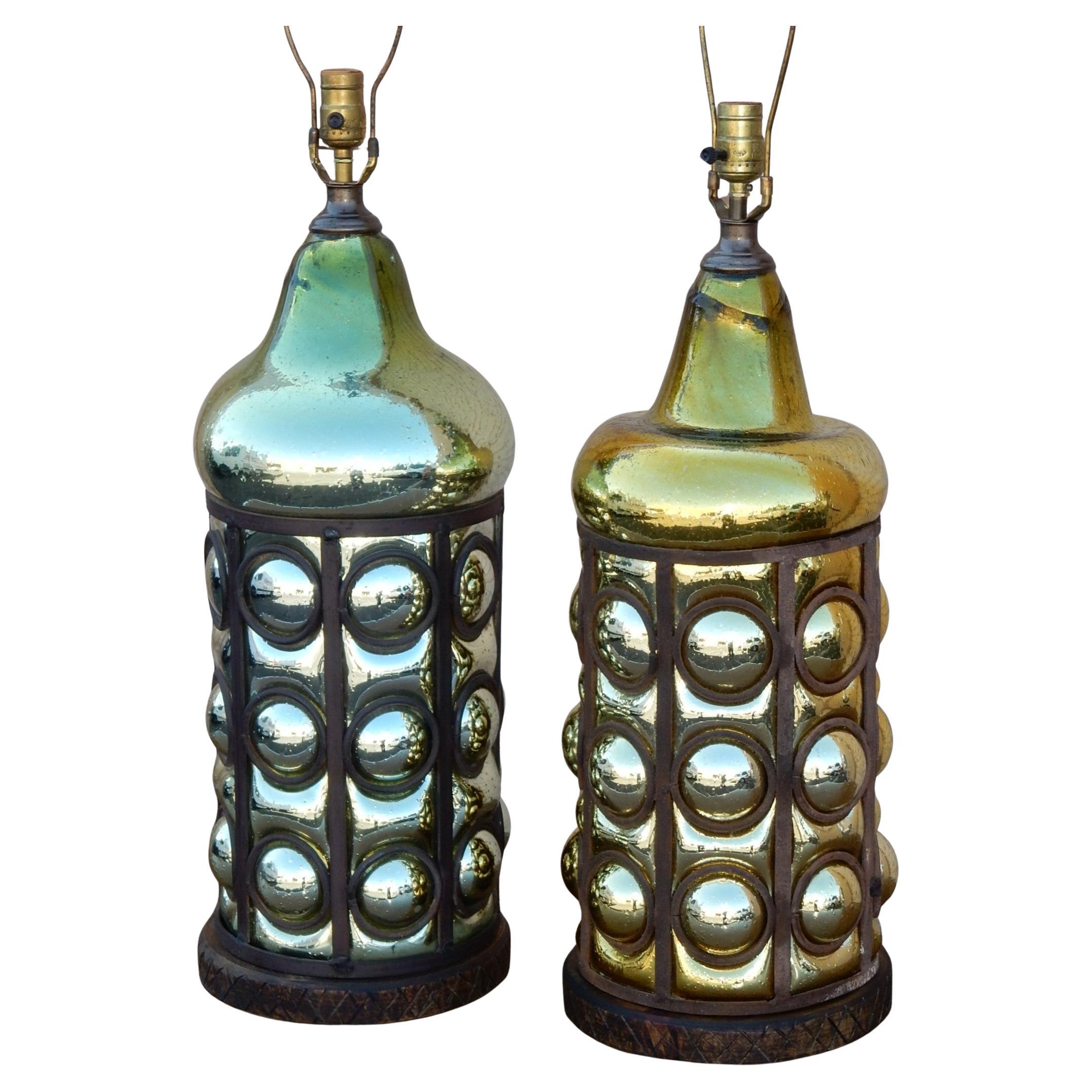 Grandi lampade da tavolo in stile Messico degli anni '50. 
Vetro soffiato spesso in una gabbia di ferro scolpito con
rivestimento in mercurio. Una è di colore oro/argento, l'altra verde/argento.
Base in Wood con design a X intorno.
Realizzato in
