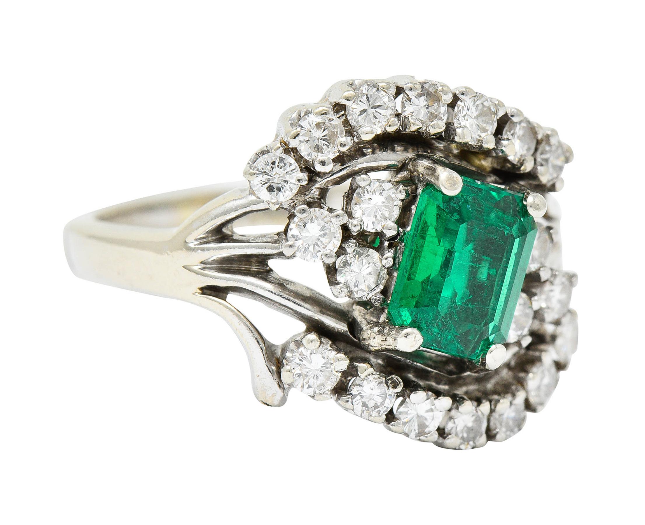 Stylized bypass ring centers an emerald cut emerald weighing approximately 0.99 carat

Strongly green in color and semi-transparent with natural inclusions

Surrounded by round brilliant cut diamonds weighing in total approximately 0.60 carat

Very
