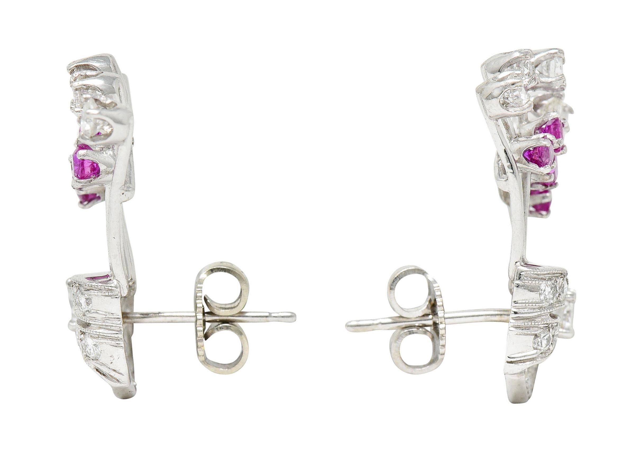 Earrings are designed as ribboned forms with gemmed extensions

Set throughout by round brilliant cut diamonds

Weighing in total approximately 1.30 carats with G to I color and SI clarity

Accented by round cut rubies weighing in total