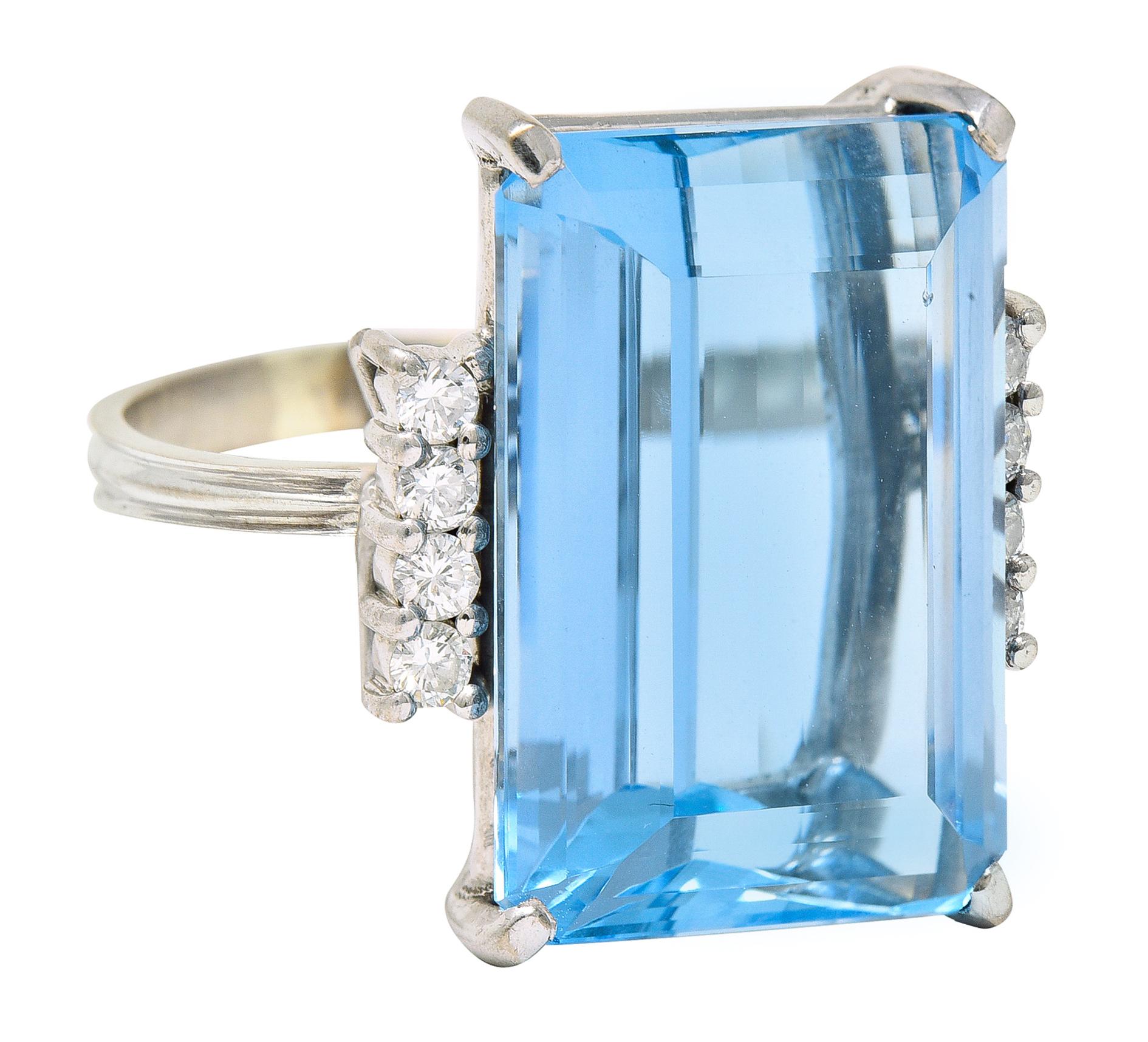 Featuring an emerald cut aquamarine weighing approximately 18.35 carats. With unique barrel faceting at crown and basket set. Transparent with vivid and uniform sky blue color - medium saturation. Flanked by rows of round brilliant cut diamonds.