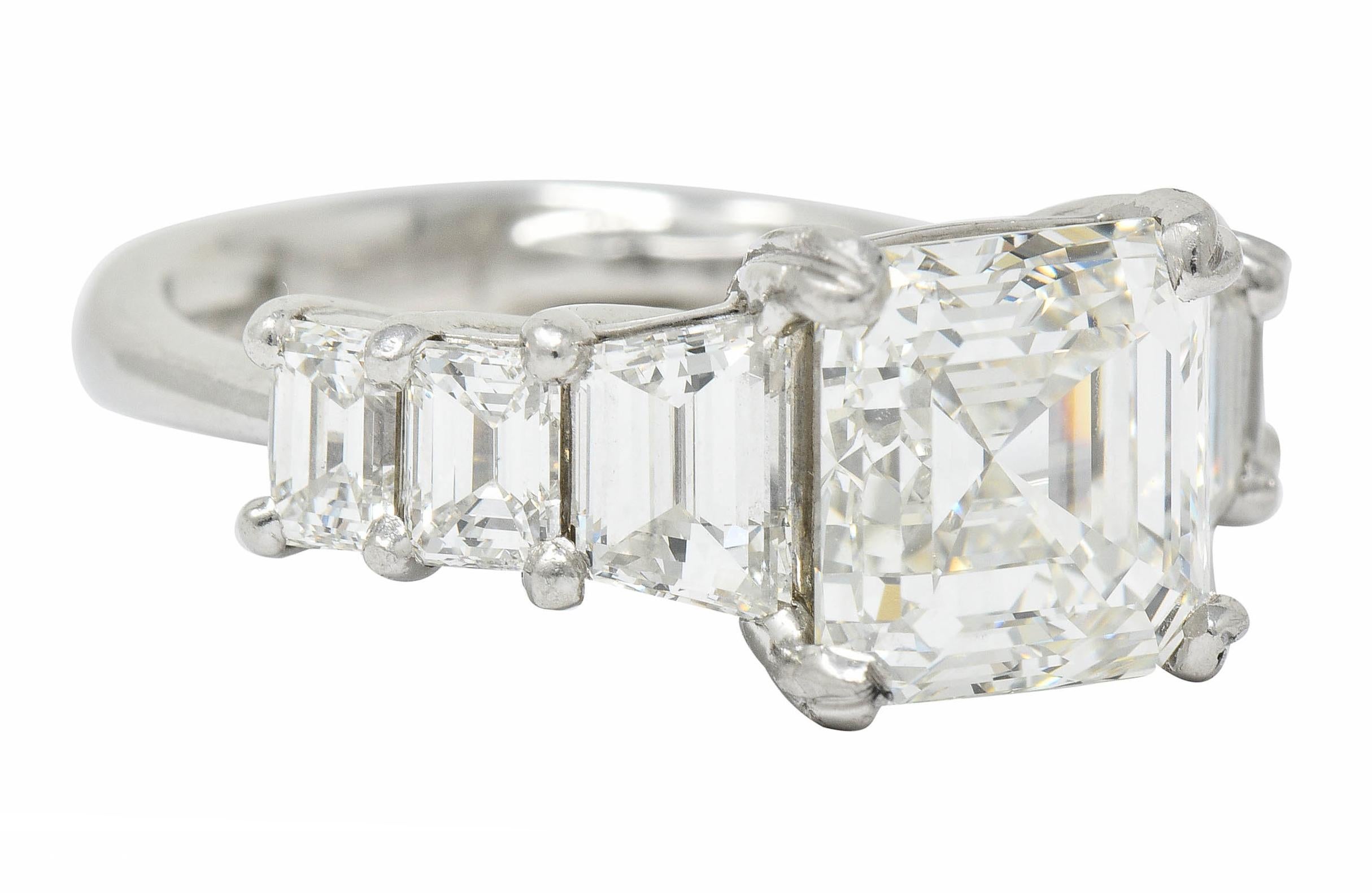 Incredible stepped mounting with a dramatically trellised gallery, basket set center, and deeply grooved decorative prongs

Featuring an asscher cut diamond weighing 3.50 carats with I color and VVS2 clarity

Flanked by trapezoid cut and baguette