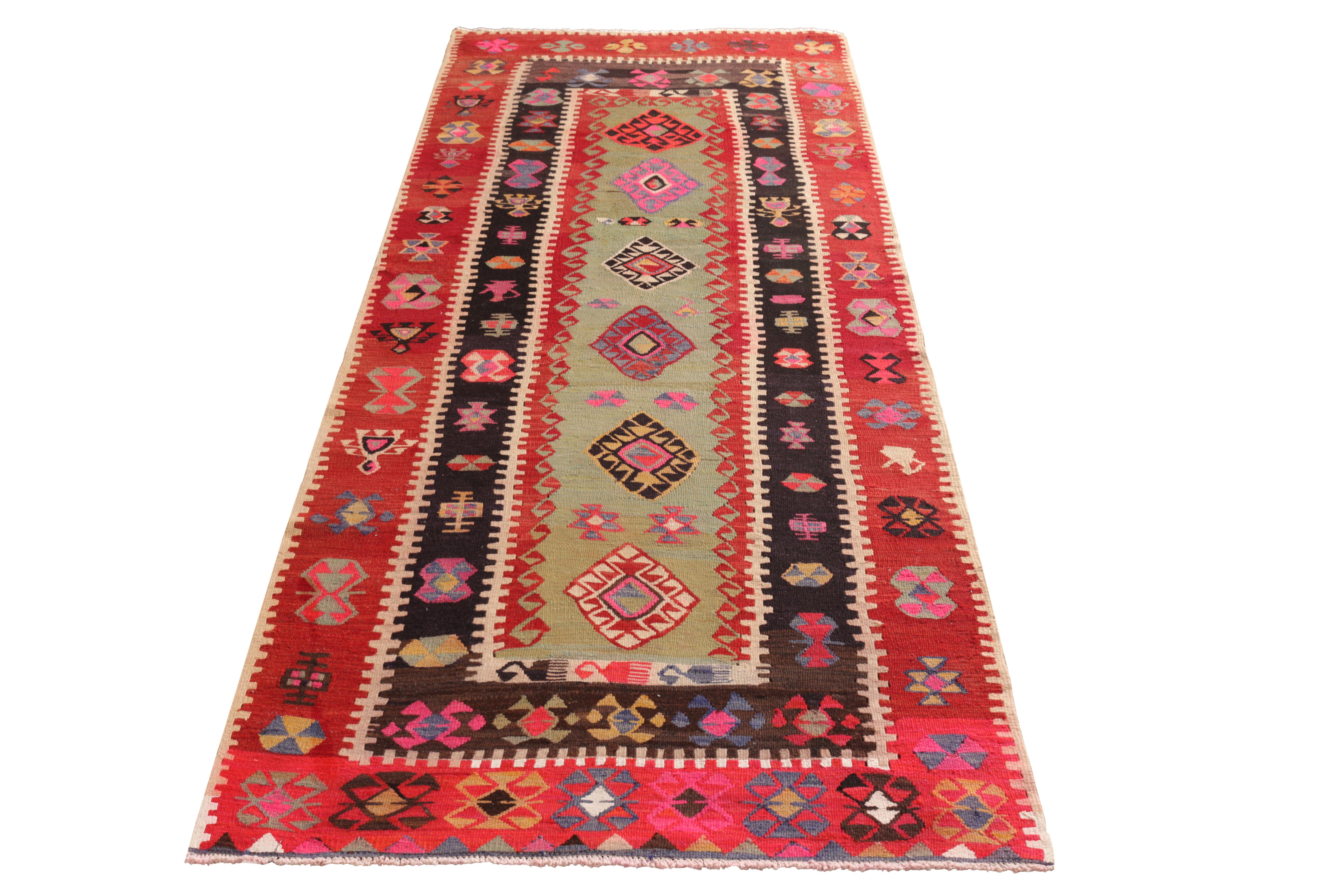 Hand knotted in wool originating from Turkey circa 1950-1960, this midcentury runner denotes a vintage Anatolian rug design, enjoying coloral tribal motifs in playful variations against prevailing, rich red and green colorway tones. Among the bright