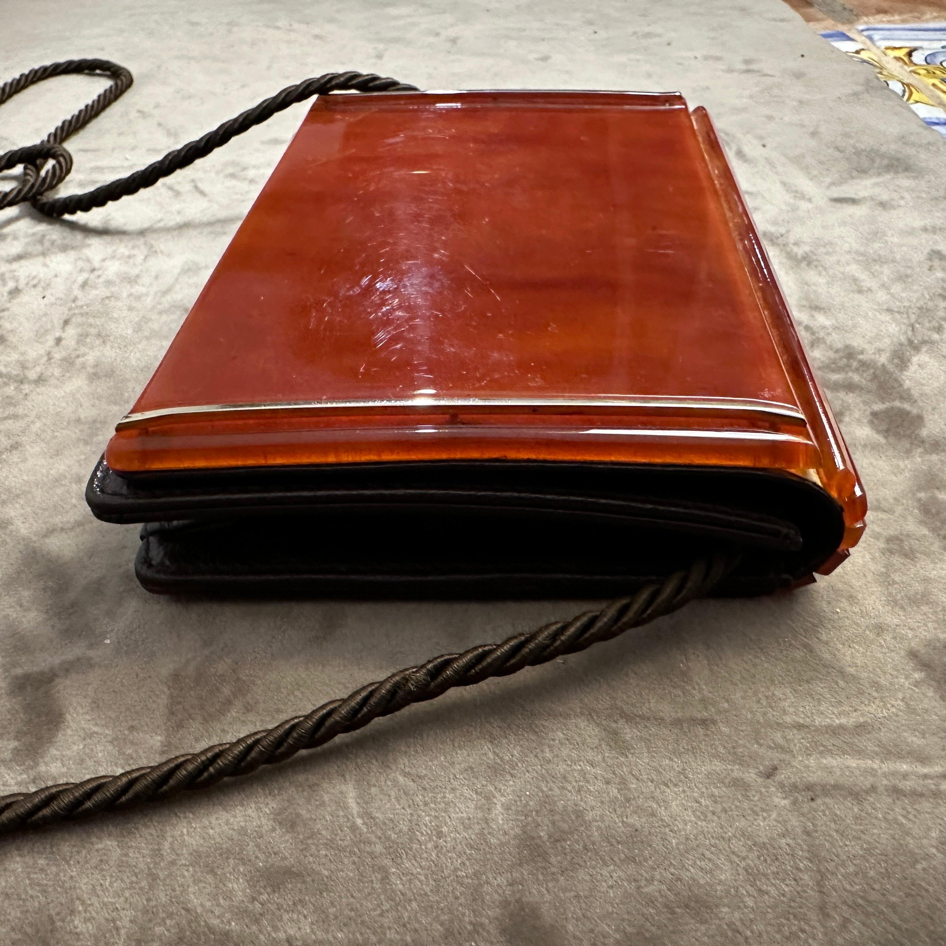 This is a 1950s Mid-Century Bakelite and Brass Italian Shoulder Mini Bag. The bag is a striking example of mid-century design, characterized by its minimalist and sleek aesthetic. It features a rectangular Bakelite body with a glossy, warm