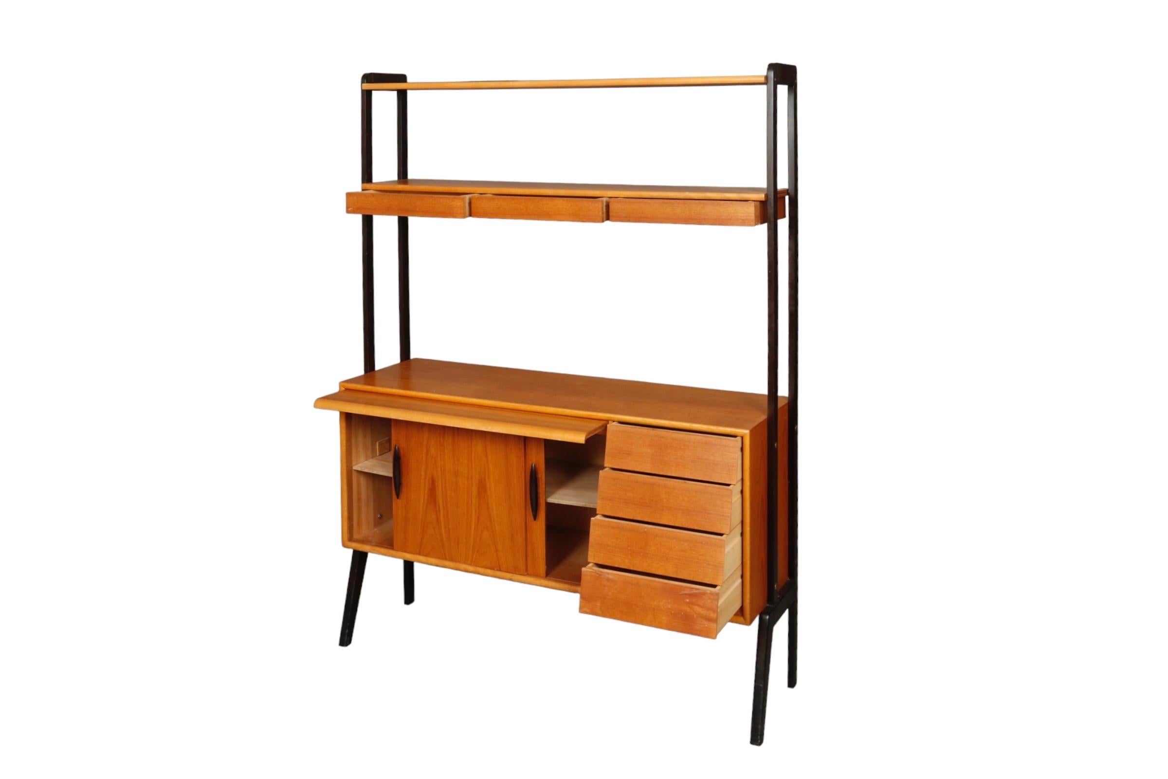 A Danish mid century bookcase with an industrial style black metal frame. Above are two shelves, one with three slender drawers, and below is a cabinet for storage with a pull out desk area. Sliding doors house a single shelf on the left and to the