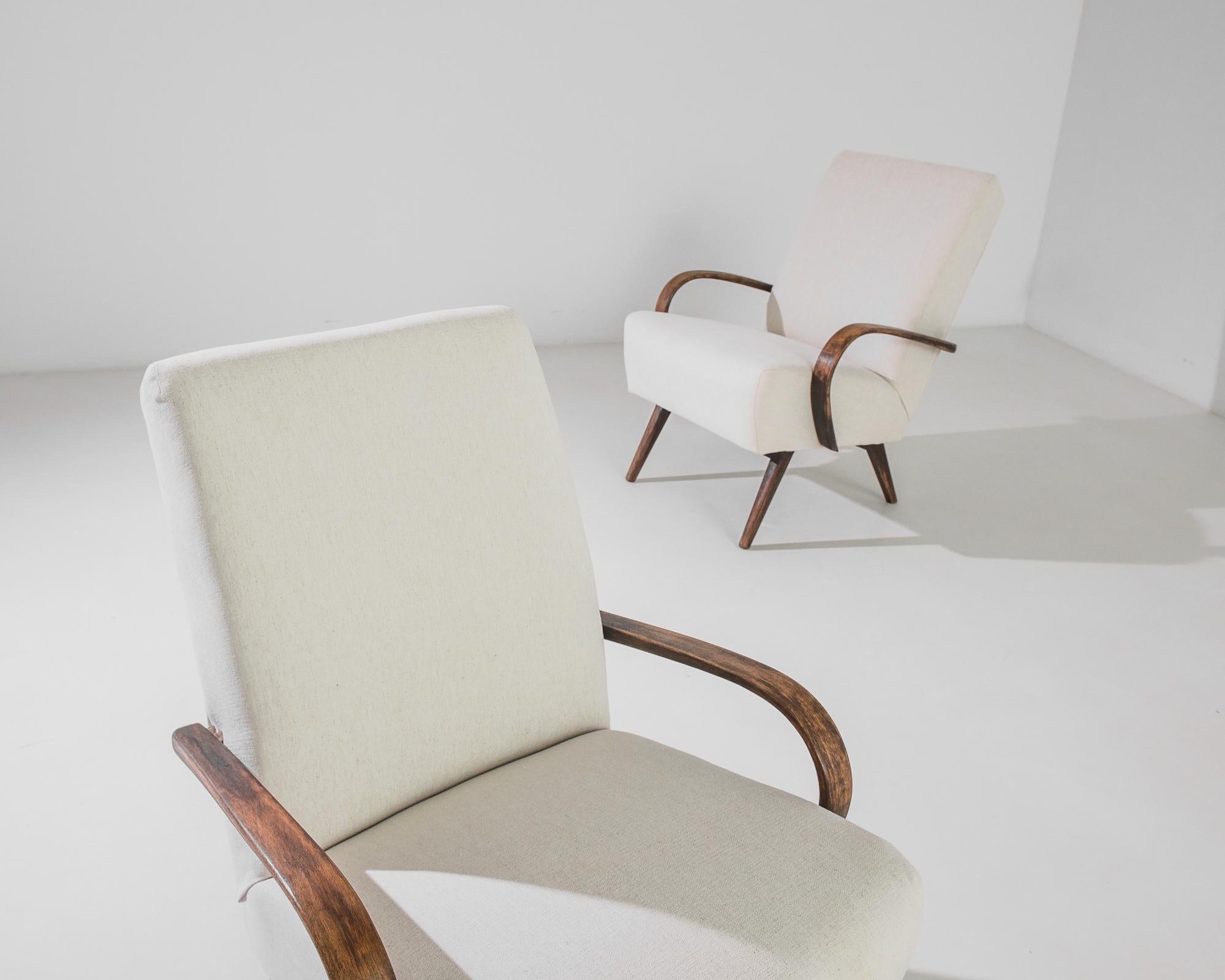 A pair of armchairs by Czech furniture designer Jindrich Halabala. This 1950s design is upholstered in an updated natural white fabric, the soothing earth tone was chosen to compliment the natural finish of the hardwood frame. Influenced by Modern