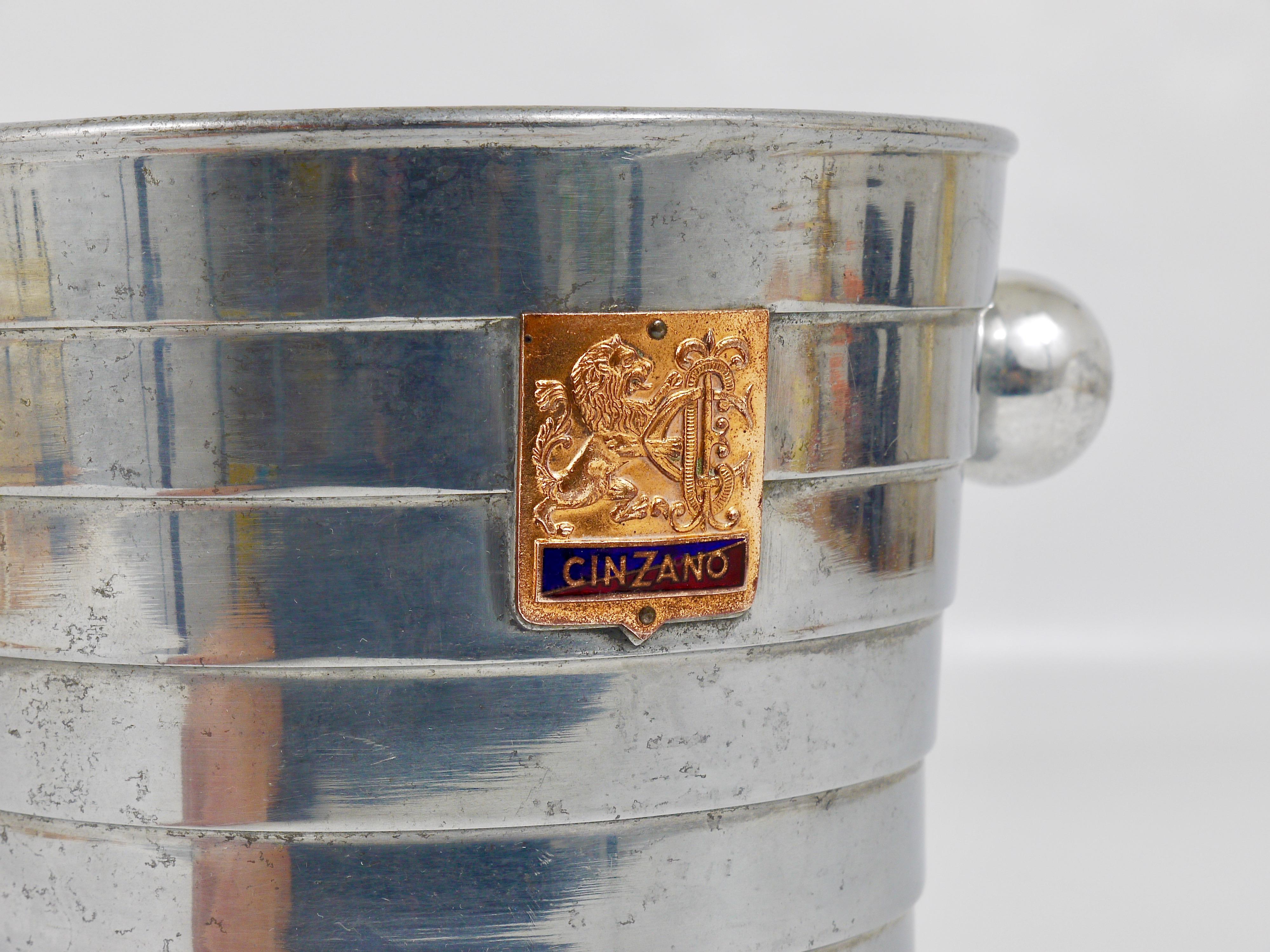 A stylish modernist Ice bucket or wine cooler from the 1950s by Cinzano. Made in Italy. Made of polished aluminum with nice ball handles and two charming enameled copper badges with the Cinzano logo. In good condition with charming patina.