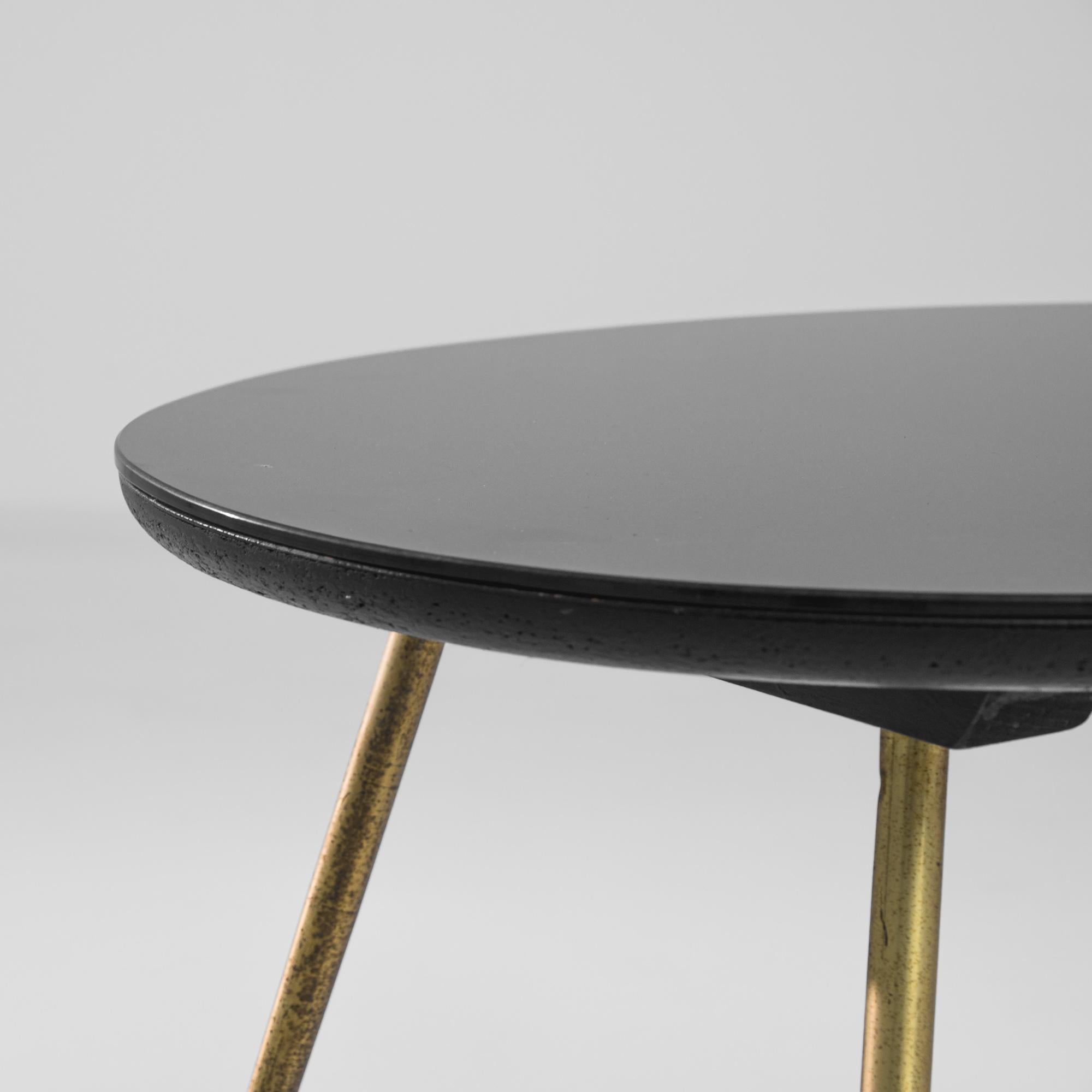 This brass coffee table was produced in France, circa 1950. A glass top is balanced upon four thin splayed brass legs, showcasing a patinated metal finish with distinct ball feet. Raised to nineteen and a half inches, the lacquered top displays a