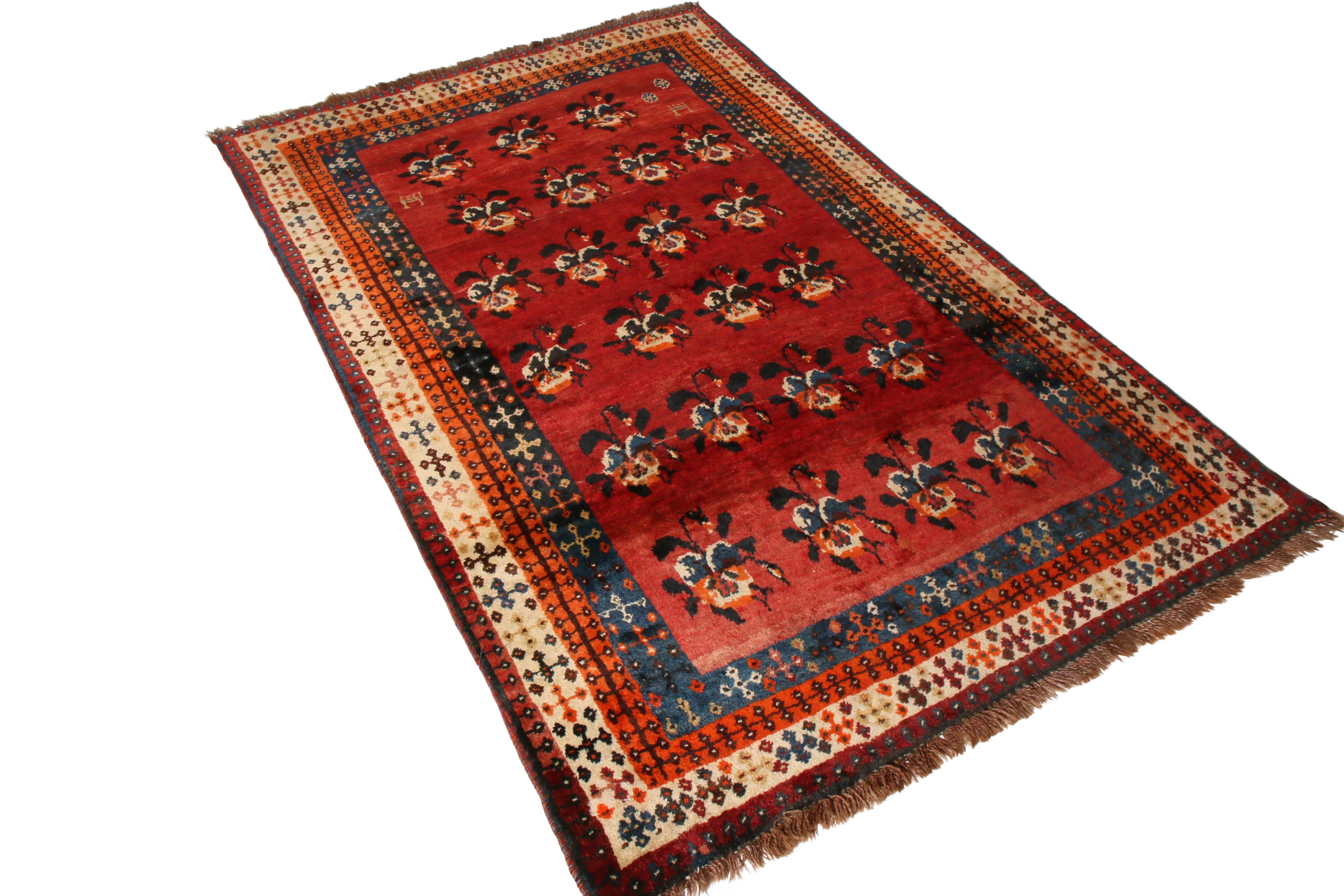Hand knotted by the Gabbeh Persian tribal weavers circa 1950-1960, this vintage midcentury floral rug enjoys a rich play of warm color and inviting repetition, juxtaposing a burnt red and deep blue colorway in the repeating floral pattern as well as