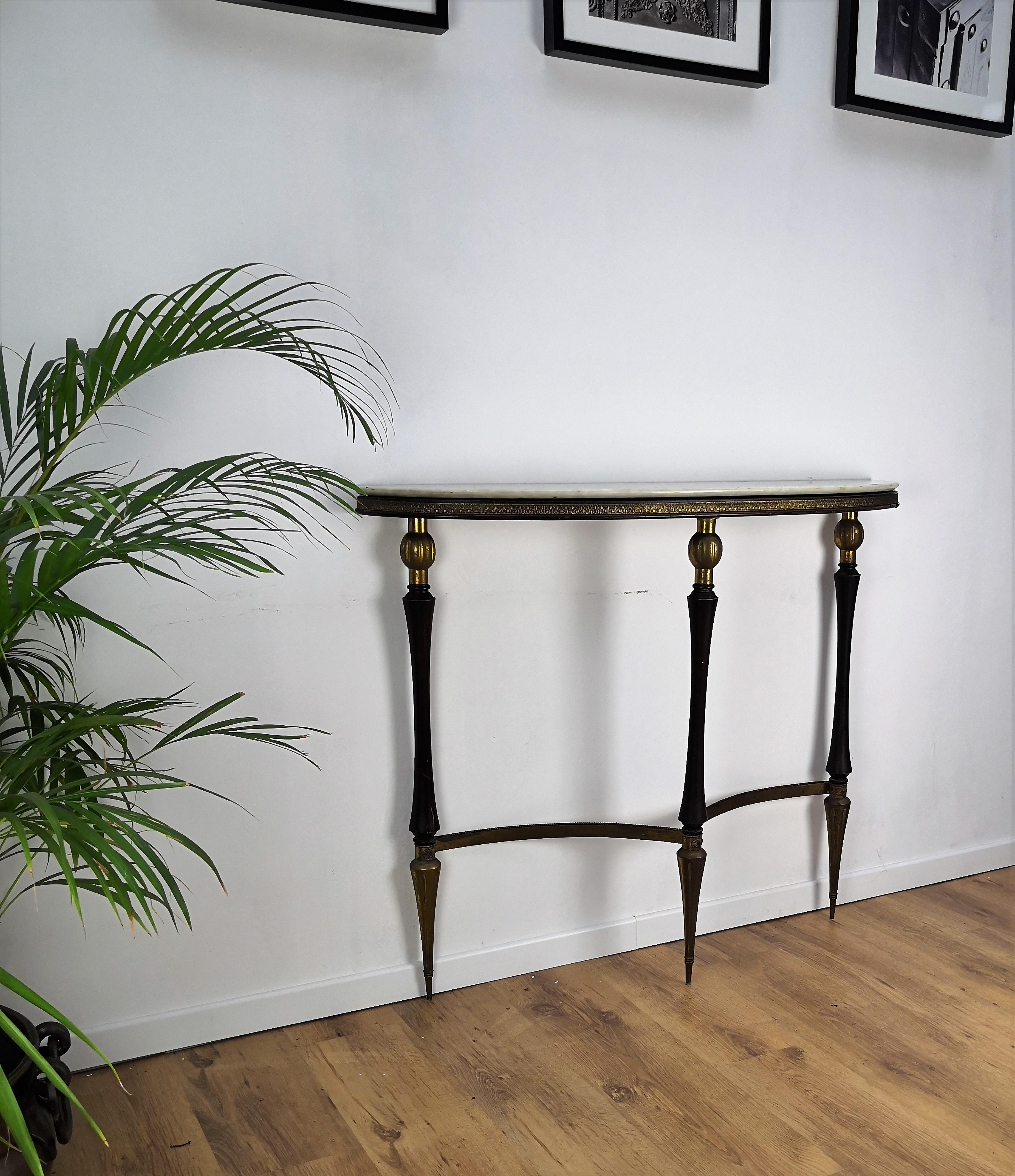 Very elegant and refined Italian 1950s Mid-Century Modern and neoclassical design demilune console table. Three stunning wood and brass round and cone shaped legs, connected to eachother in curved brass and with its typical marble top give this