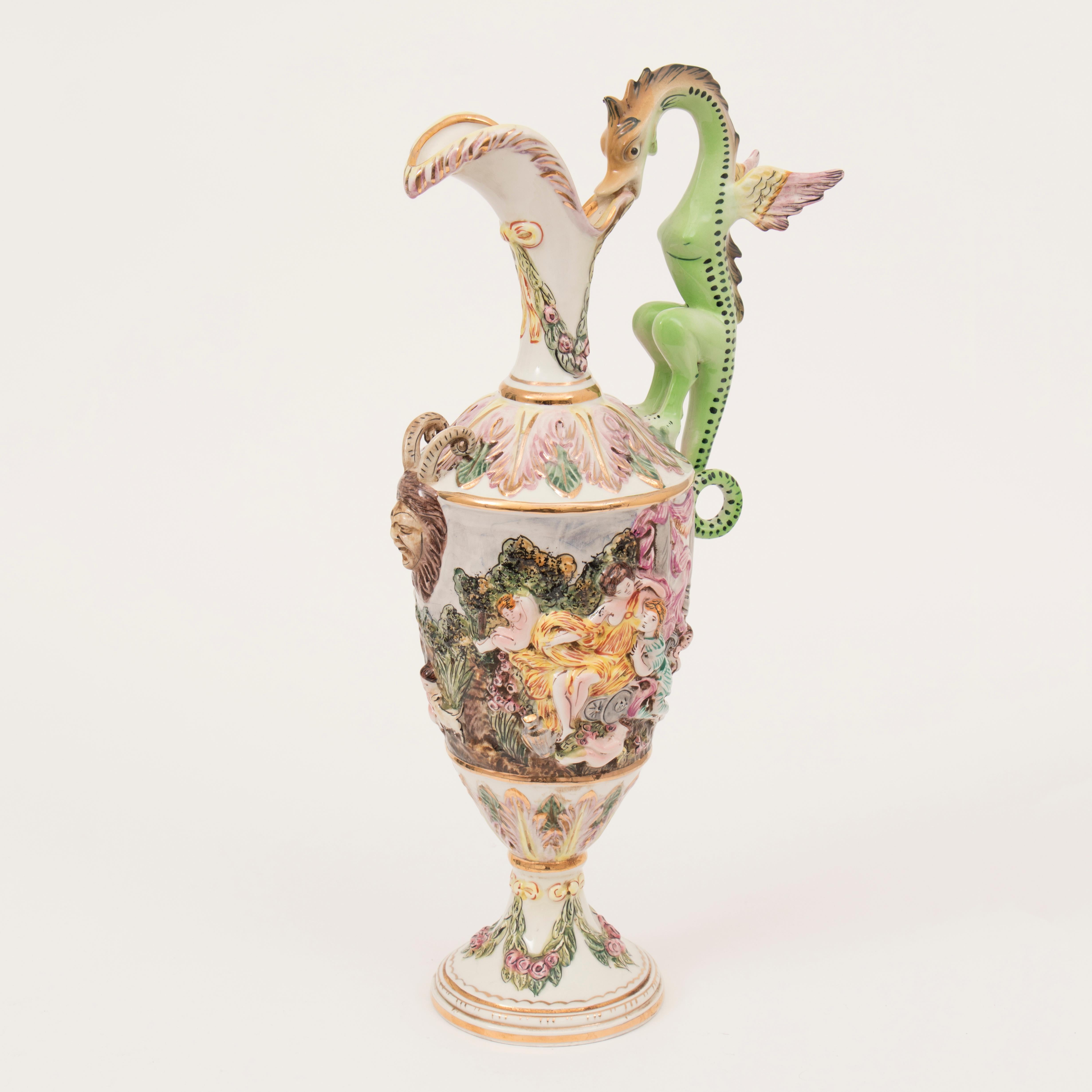 A 1950s vintage large Italian Capodimonte porcelain pitcher with an ornate winged dragon handle. The pitcher features a colourful mythological garden scene with cherubs, robed ladies, animals and children. A feature Greek Satyr head and horns are on