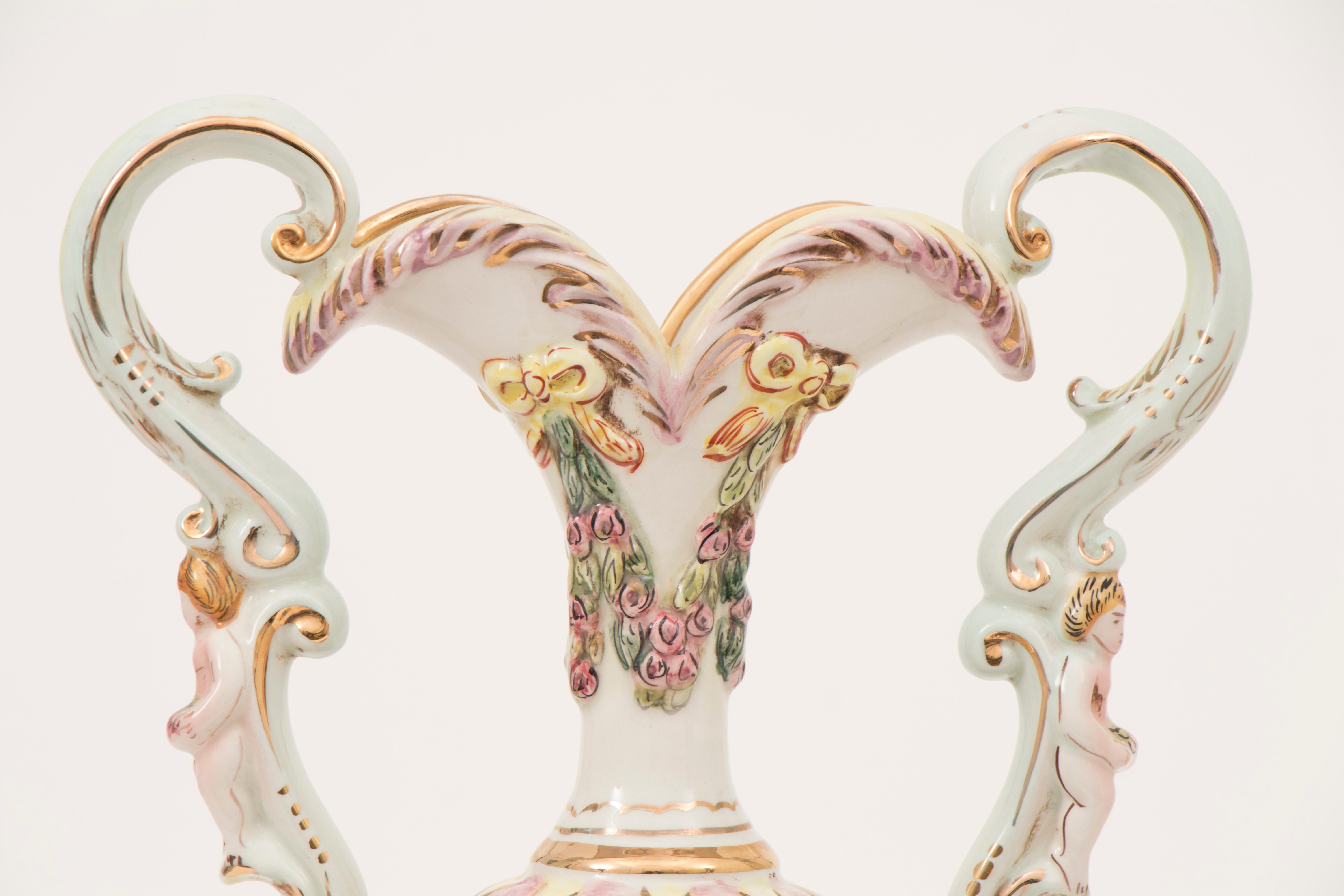 A vintage 1950s large Italian Capodimonte porcelain two-handled urn with a cherub on each ornate handle. The urn features a colourful mythological garden scene with cherubs, men and women, children and garden furniture. A feature Greek Satyr head is