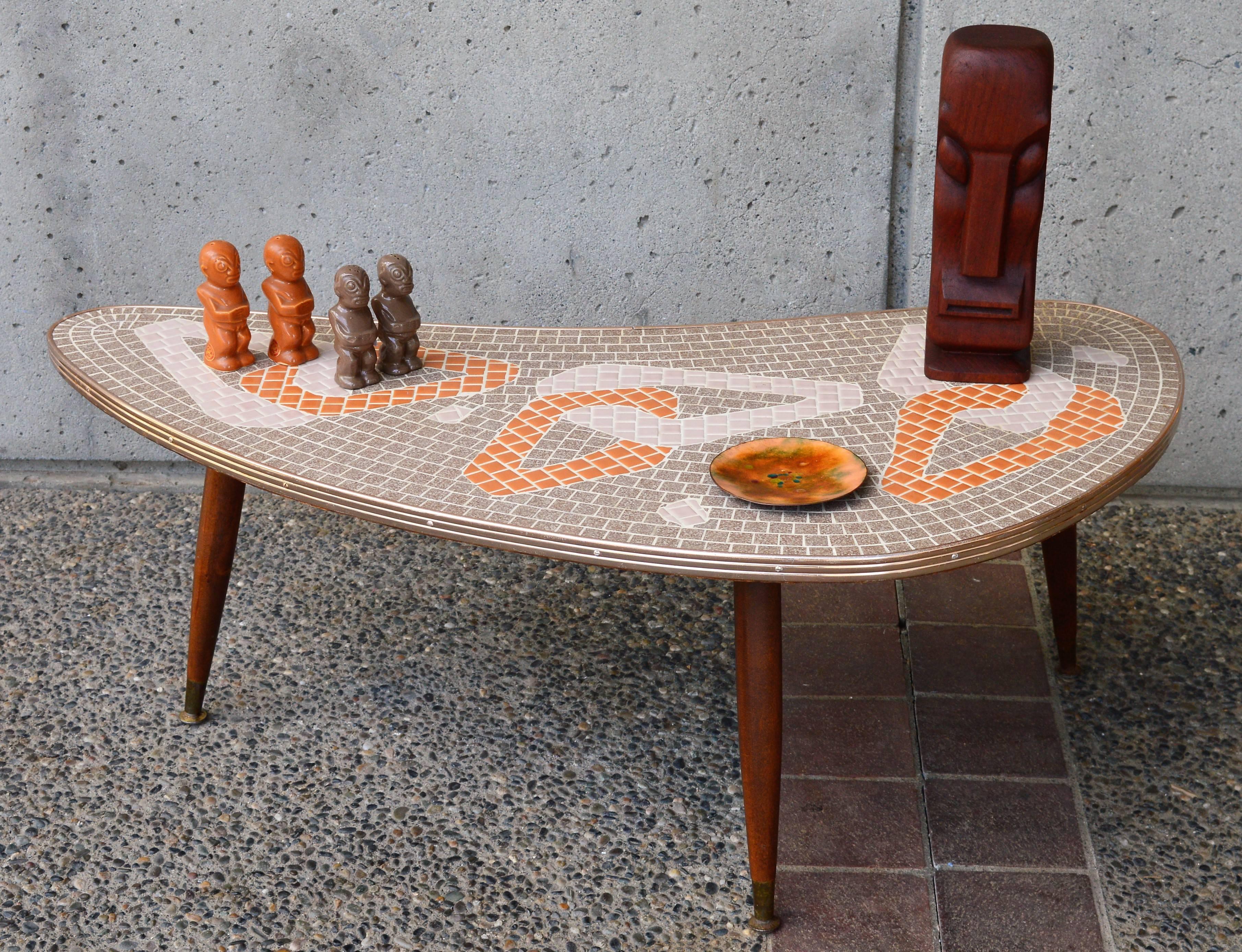 This totally rare and fabulous 1950s Mid-Century Modern Atomic era boomerang coffee table has a striking tile mosaic top with a chain link pattern in ecru, cream and burnt orange. Finished with a pink copper toned metal edging and three splayed