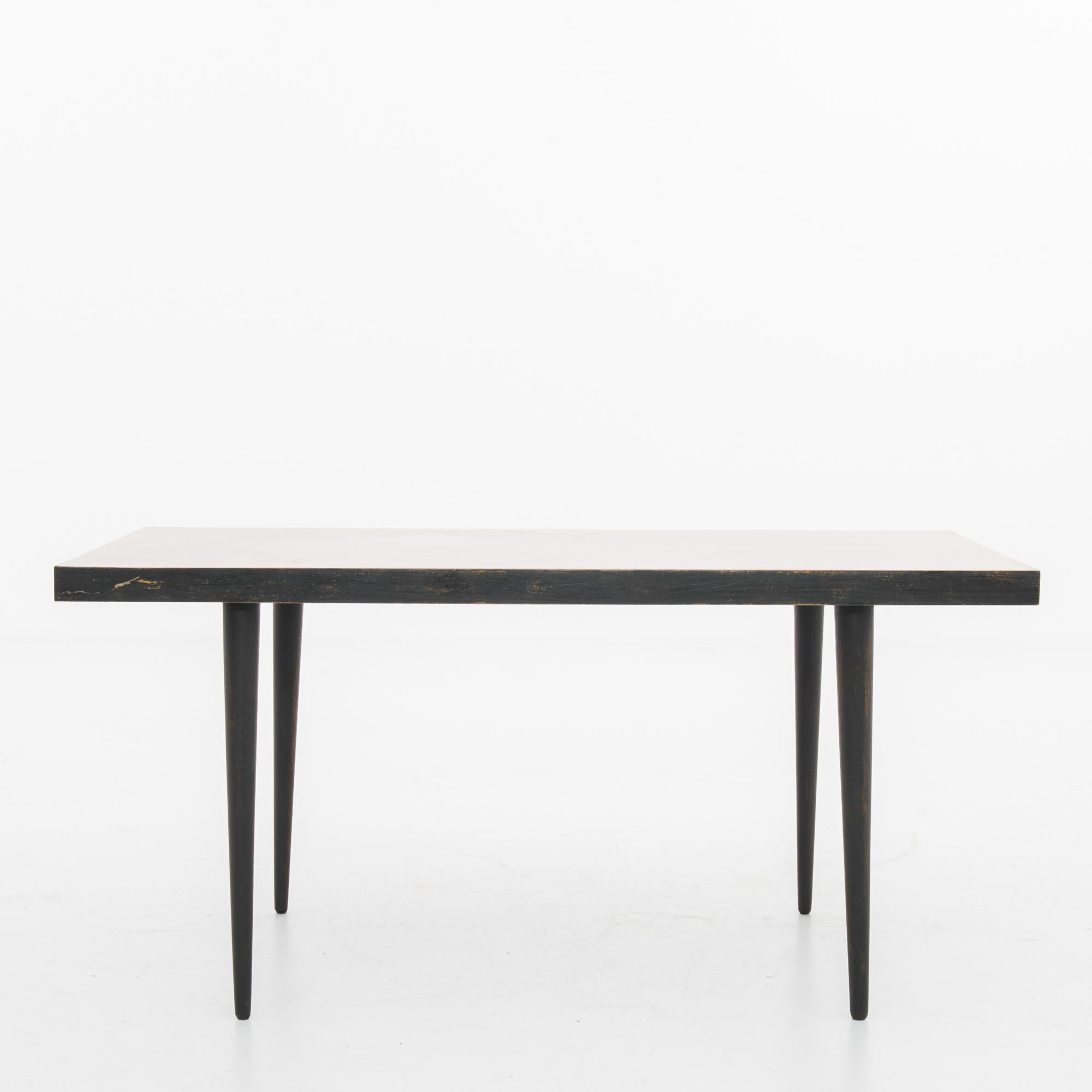 A wooden coffee table from 1950s Czechia. A stylish Mid-Century Modern design: the rectangular table top sits atop four tapered legs for a clean, Minimalist Silhouette. The legs and profile of the table top are painted black, creating a sleek