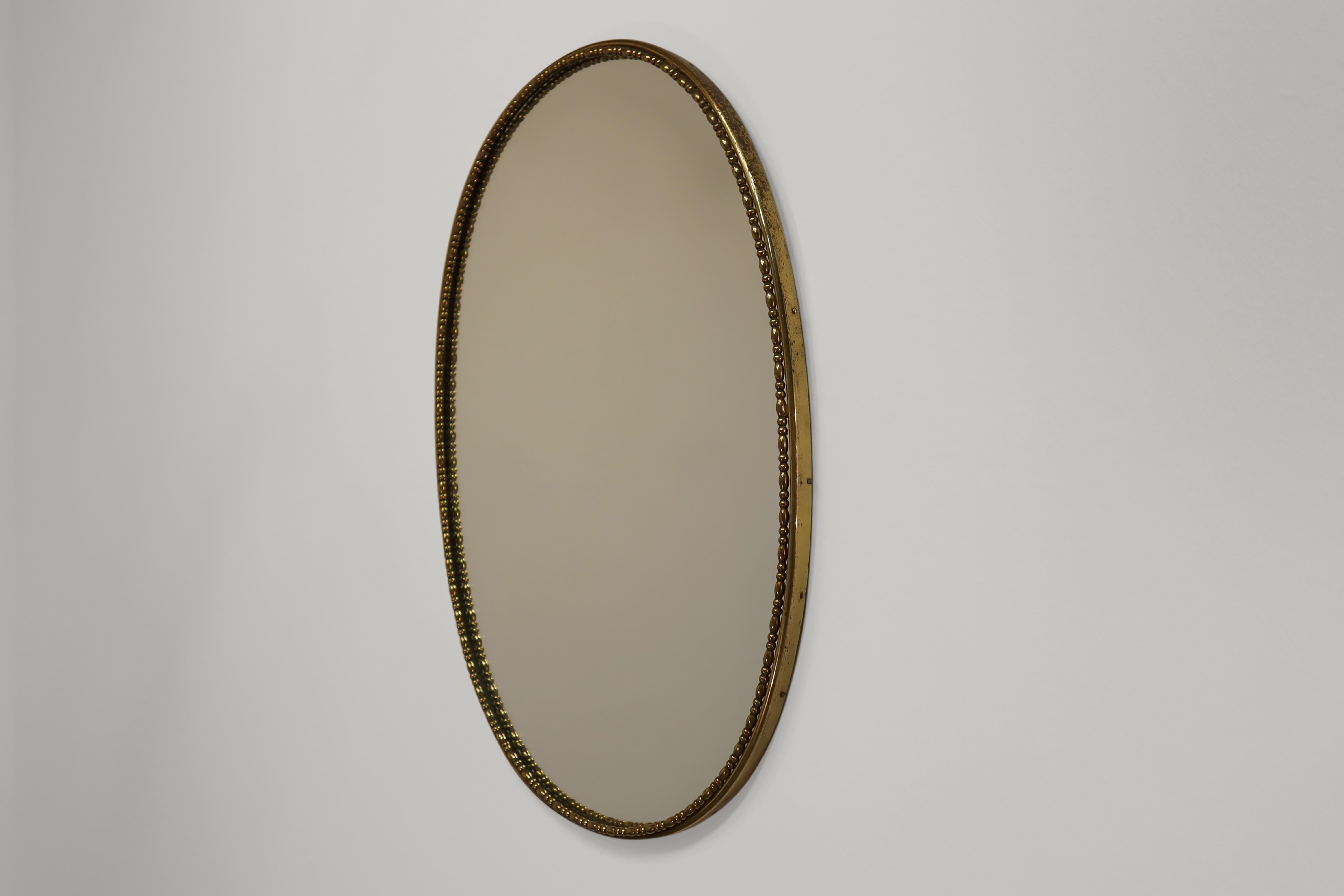 Mid-Century Modern oval-shaped wall mirror in patinated brass. Made in Italy in 1950s.

This mirror is constructed in wood, with a brass lip wrought around the perimeter and holding the mirror in place. Brass screws fix the brass lip to the wood