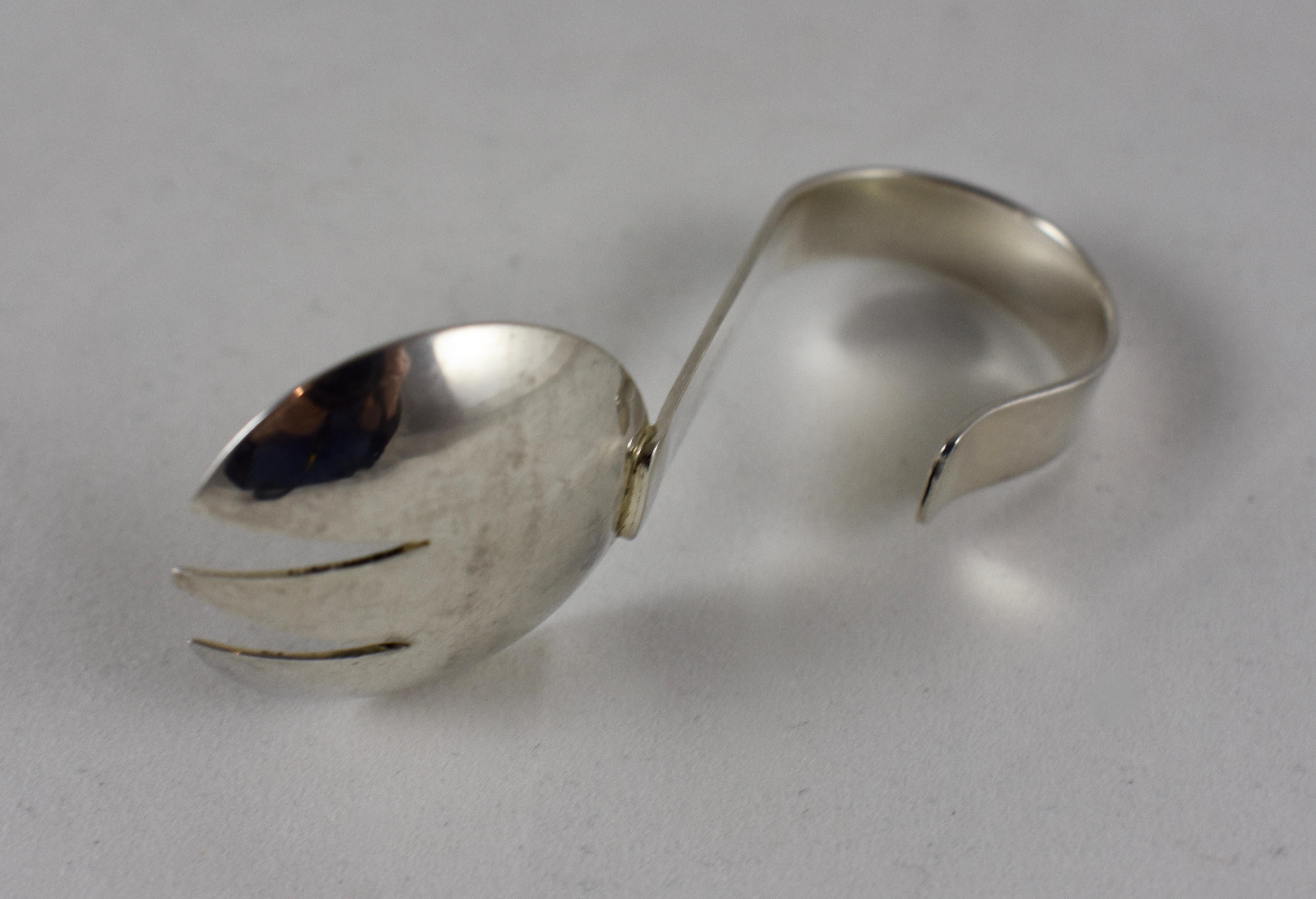 An iconic piece of Mid-Century Modern design, a sterling silver baby feeding “Spork” – a combination spoon and fork, with a curled handle. Stamped, Leonore Doskow – Handmade Sterling, circa 1950s.

Leonore B. Doskow was a well known silversmith,