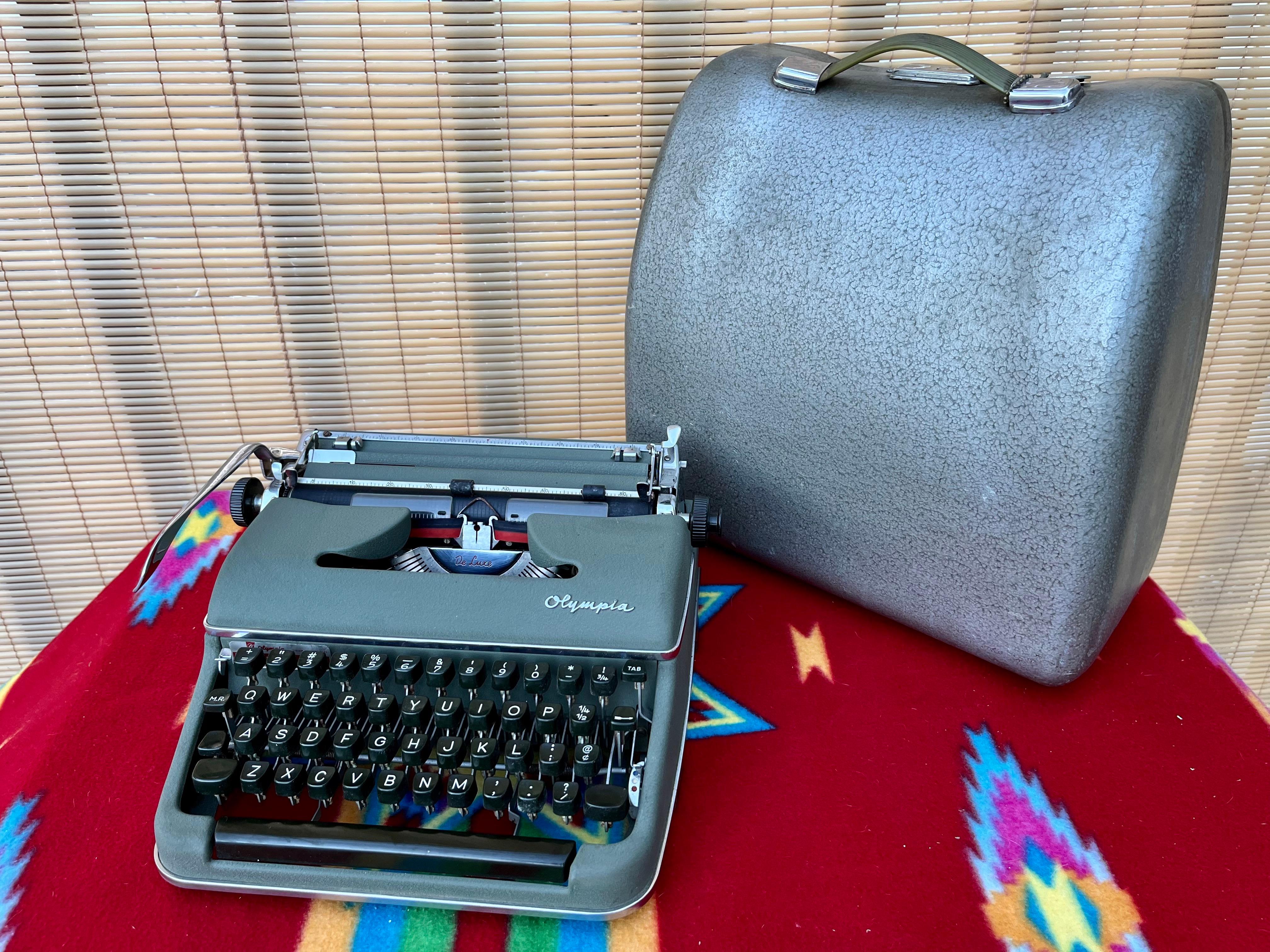 Vintage Mid-Century Modern Olympia SM3 portable typewriter with the original metal case. Circa 1950s. 
Features a Qwerty keyboard, a grayish green color body with chrome trims and the original metal case with a galvanized-like finish and the