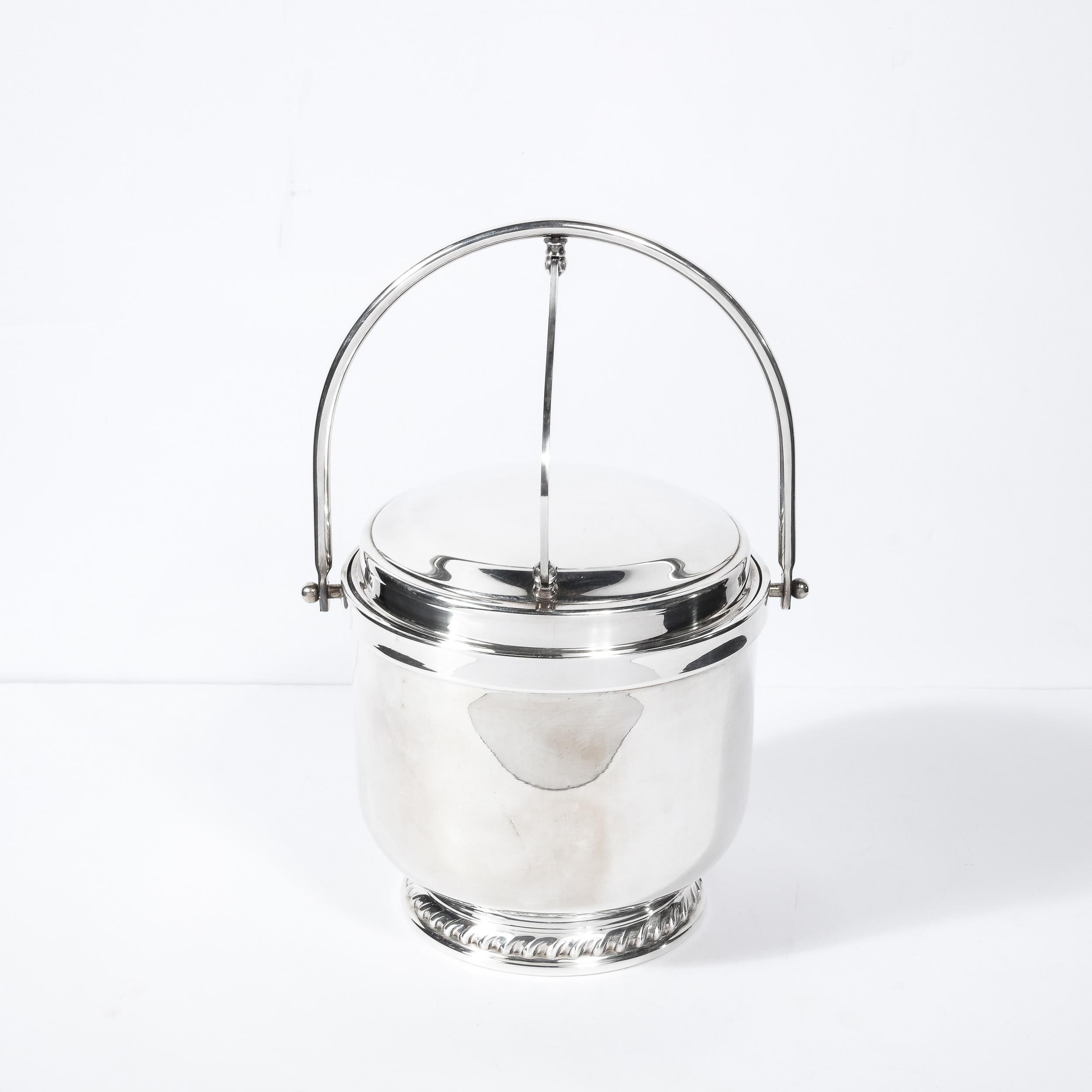 This beautiful Mid-Century Modern silverplate ice bucket was realized in the United States circa 1950. It features a circular base with amorphic stylized tear drop detailing in relief that ascends into a cylindrical body culminating in a stepped