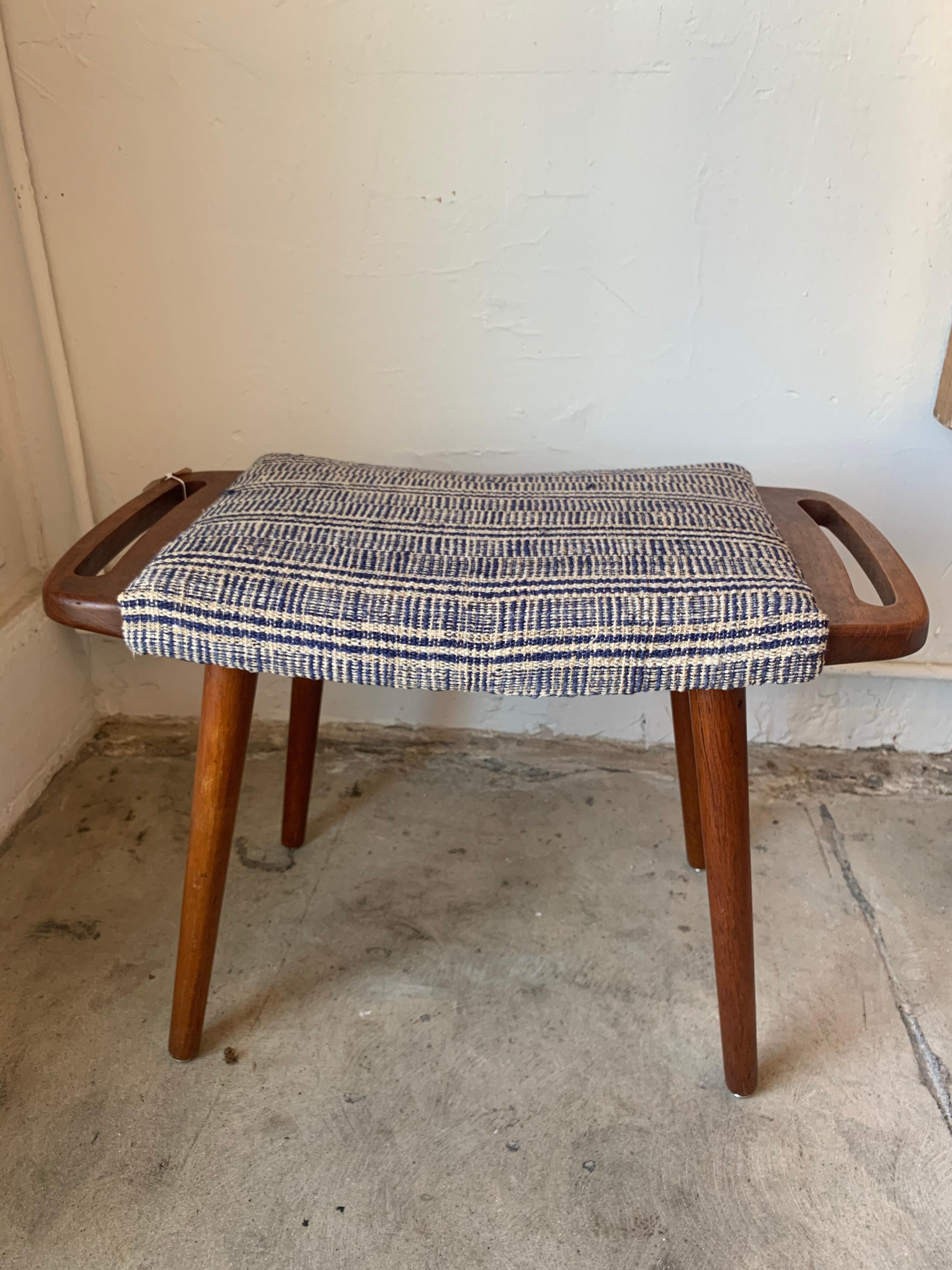 Offered is a vintage ottoman in style of the renowned designer Hans Wegner, designed in 1951. Made of solid teak and upholstered with a textured stripped fabric that is in great condition.