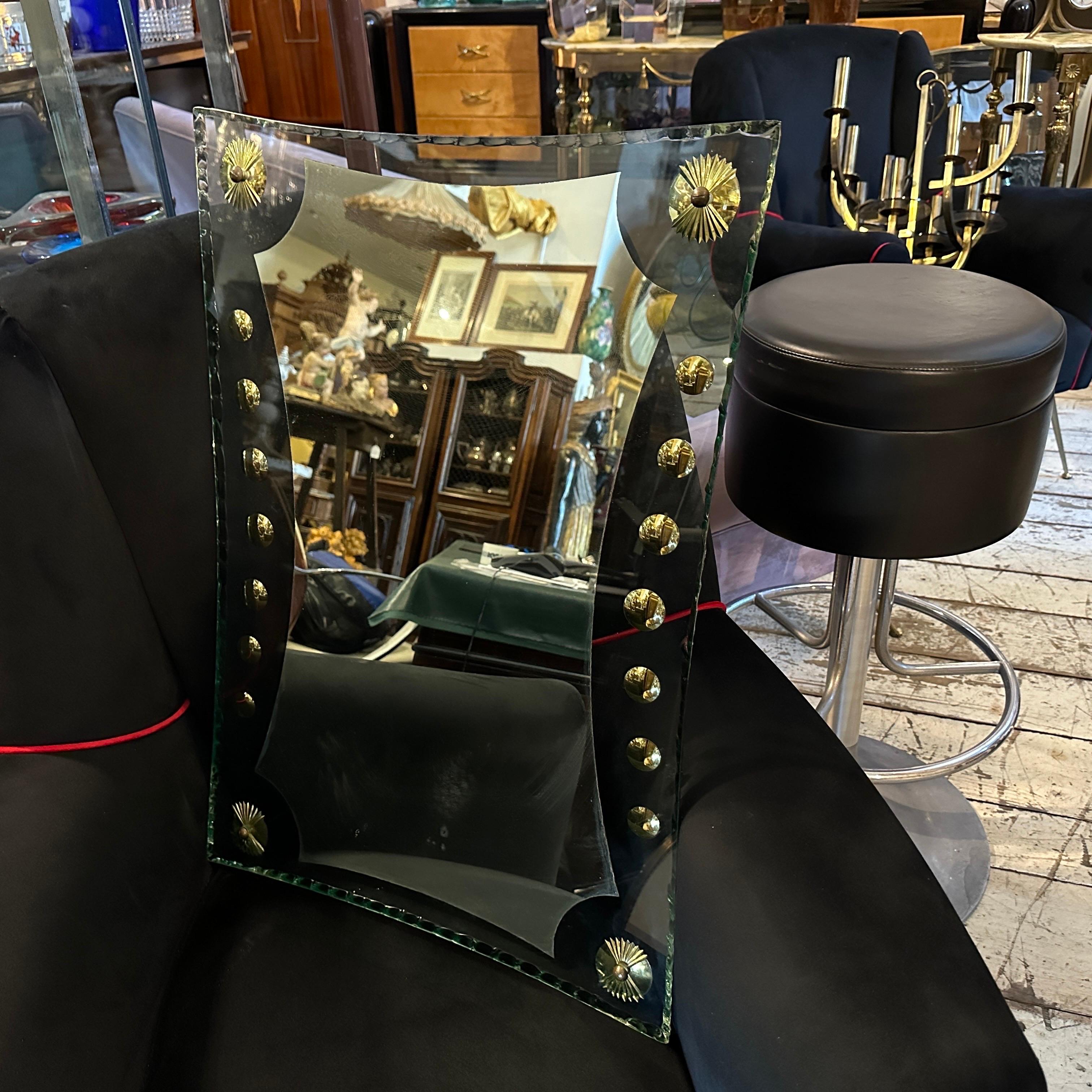 This 1950s Mid-Century Modern Verde Nilo Glass and Brass Wall Mirror by Cristal Arte is a beautiful and elegant decorative item. Its unique shape, high-quality materials, and intricate brass details make it a standout piece that captures the essence