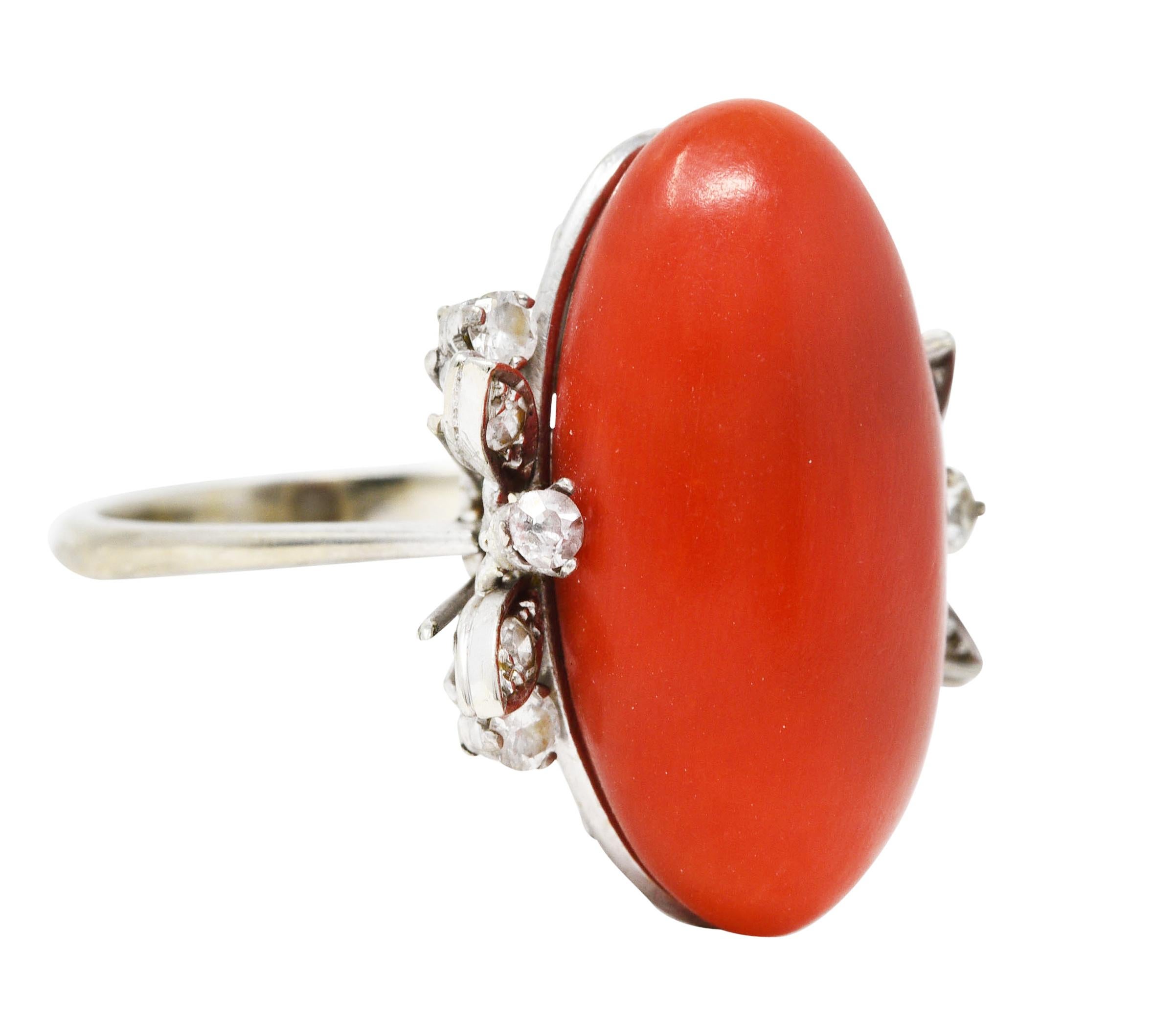 Featuring an elongated oval cabochon of coral - opaque and medium light red in color

Measuring approximately 23.0 x 12.5 mm

Flanked by clustered shoulders comprised of single and round brilliant cut diamonds

Weighing in total approximately 0.30