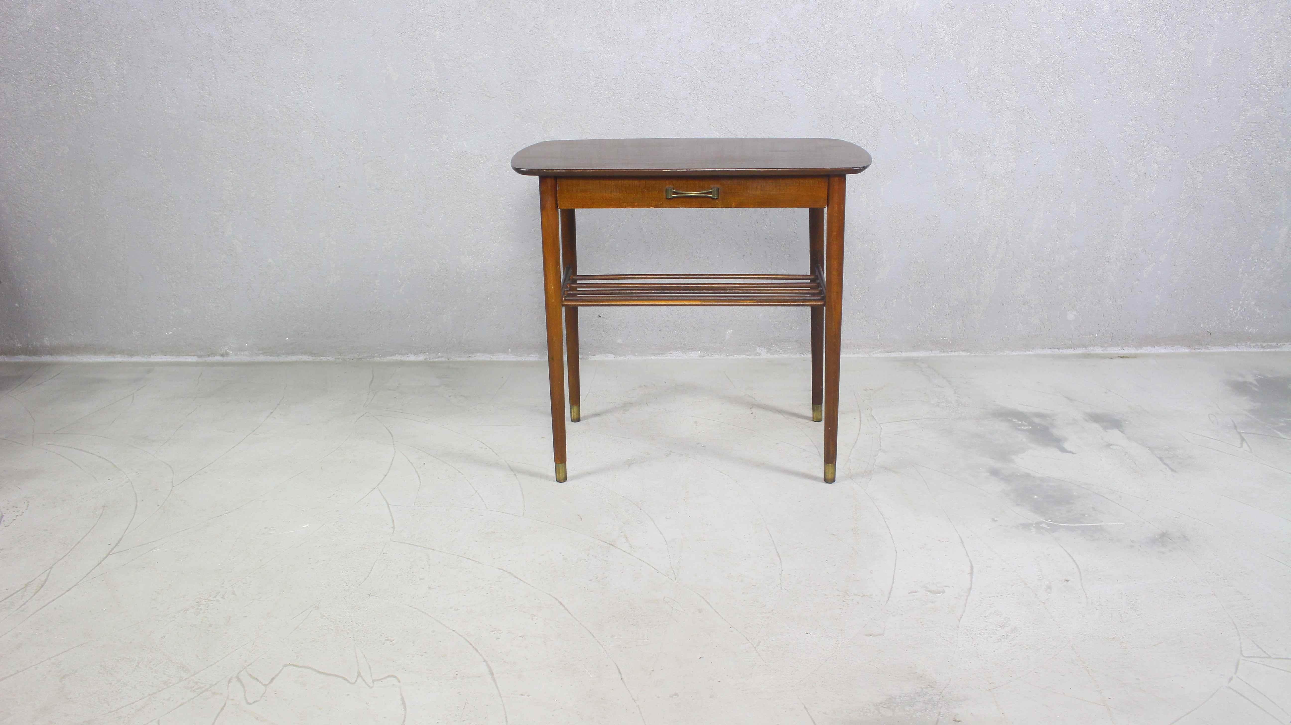 Vintage Mid-Century Modern brass feet side table.
Item features metal capped brass plated feet, lower shelf, beautiful wood grain.
Under the tabletop, a drawer with a brass handle.