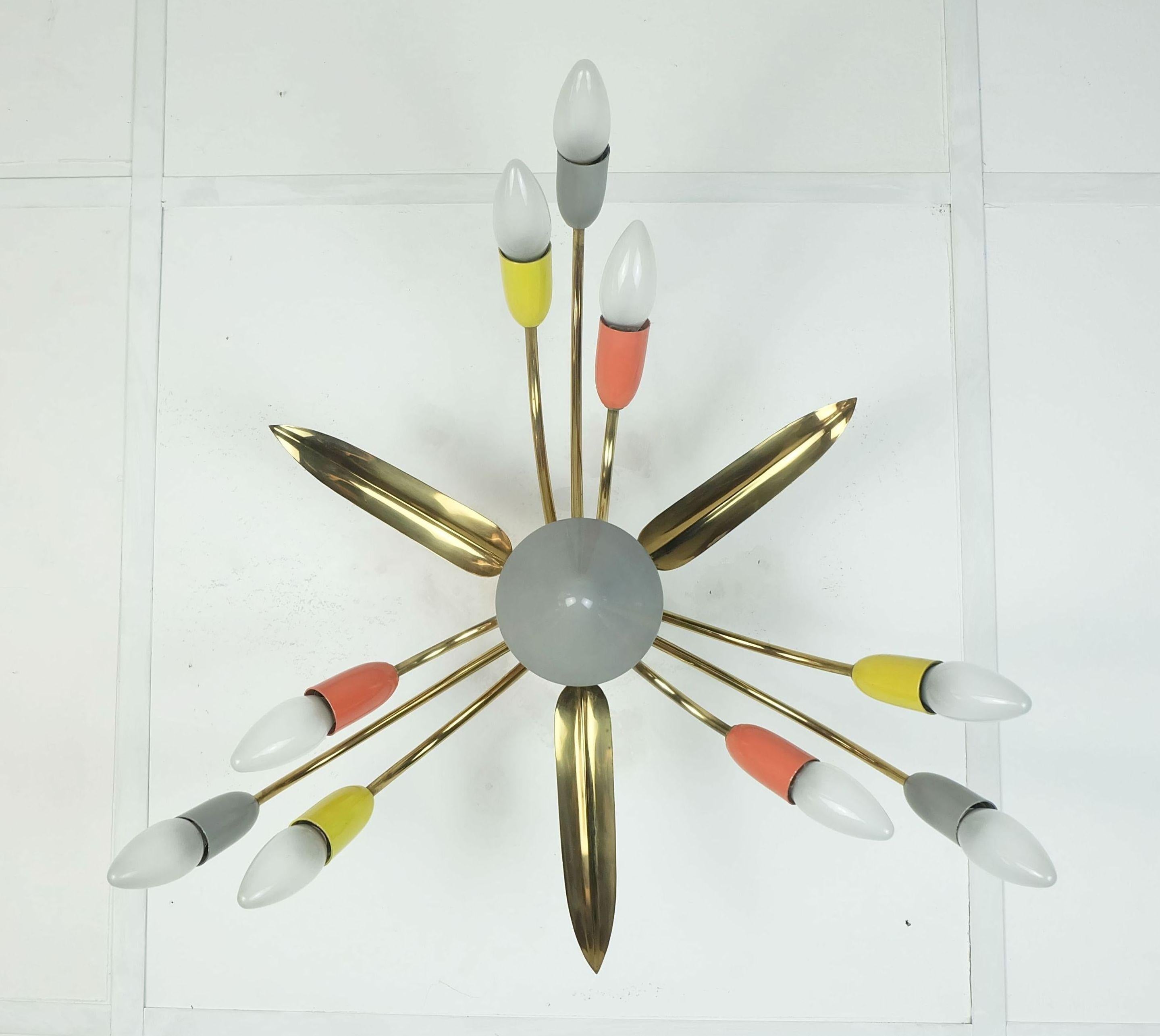 Amazing 1950s mid century sputnik ceiling light. The frame and canopy are made of brass. The lamp has nine arms, each with three gray, red, or yellow painted metal spouts above the sockets. Leaf-shaped decorative elements made of brass are located