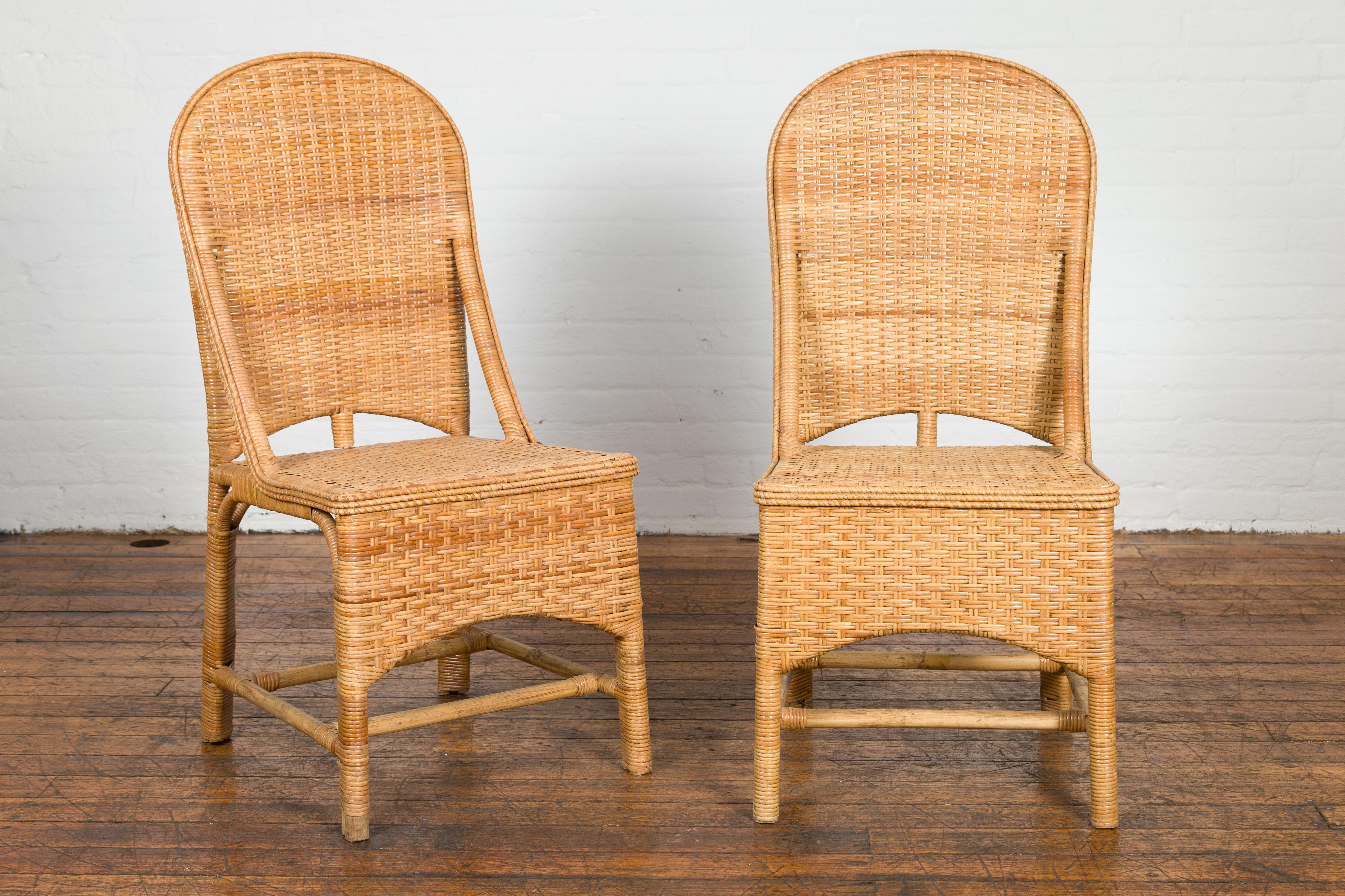 A pair of vintage Country style hand woven rattan chairs from the mid 20th century, with arching backs and double H-Form cross stretchers. Embrace a fusion of functionality and earthy aesthetics with these vintage, mid-20th-century rattan chairs.