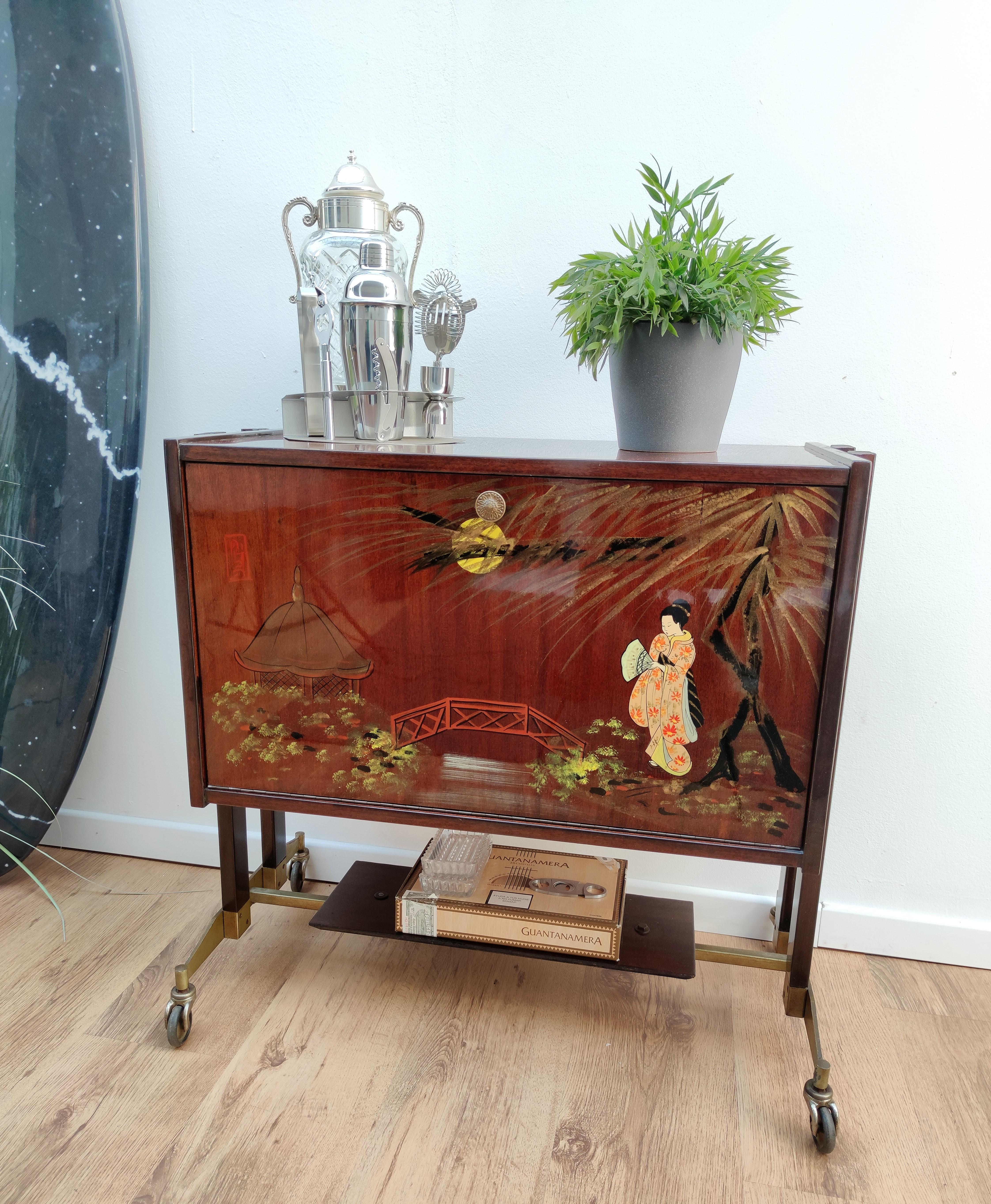 Very elegant Italian Art Deco Mid-Century Modern dry bar cabinet cart characterized by its original Asian themed painted front wood pull-out tilt door with interior part in mirror glass, standing on its antique brass wheels.

This charming piece