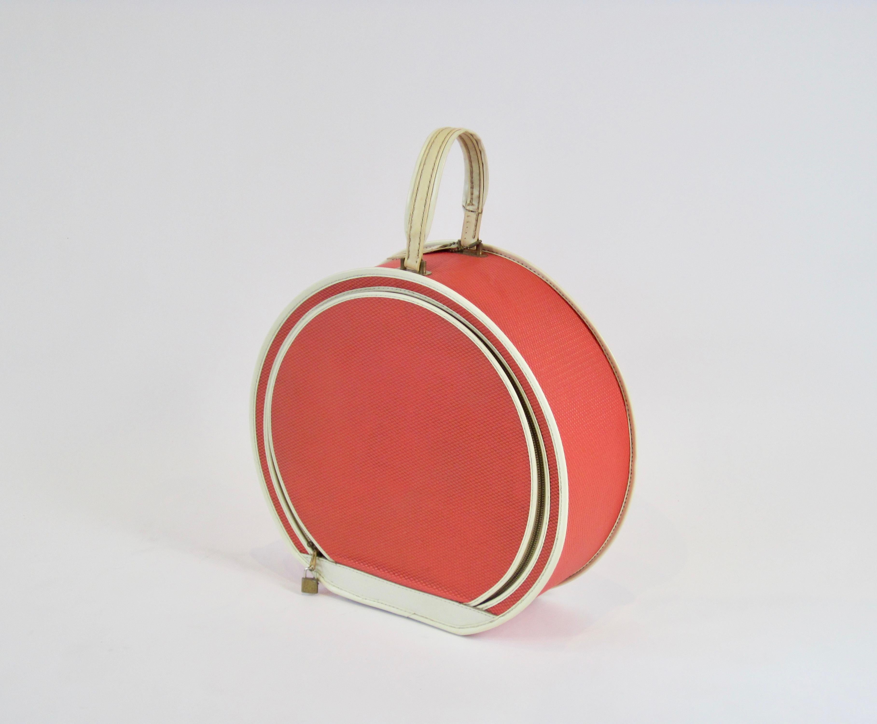 Mod 1950s round hat box/train case by Leeds Tested Travelwear New York. The coral-red textured exterior is a gorgeous pop of color with white piping and brass hardware details.  An excellent prop or display piece.