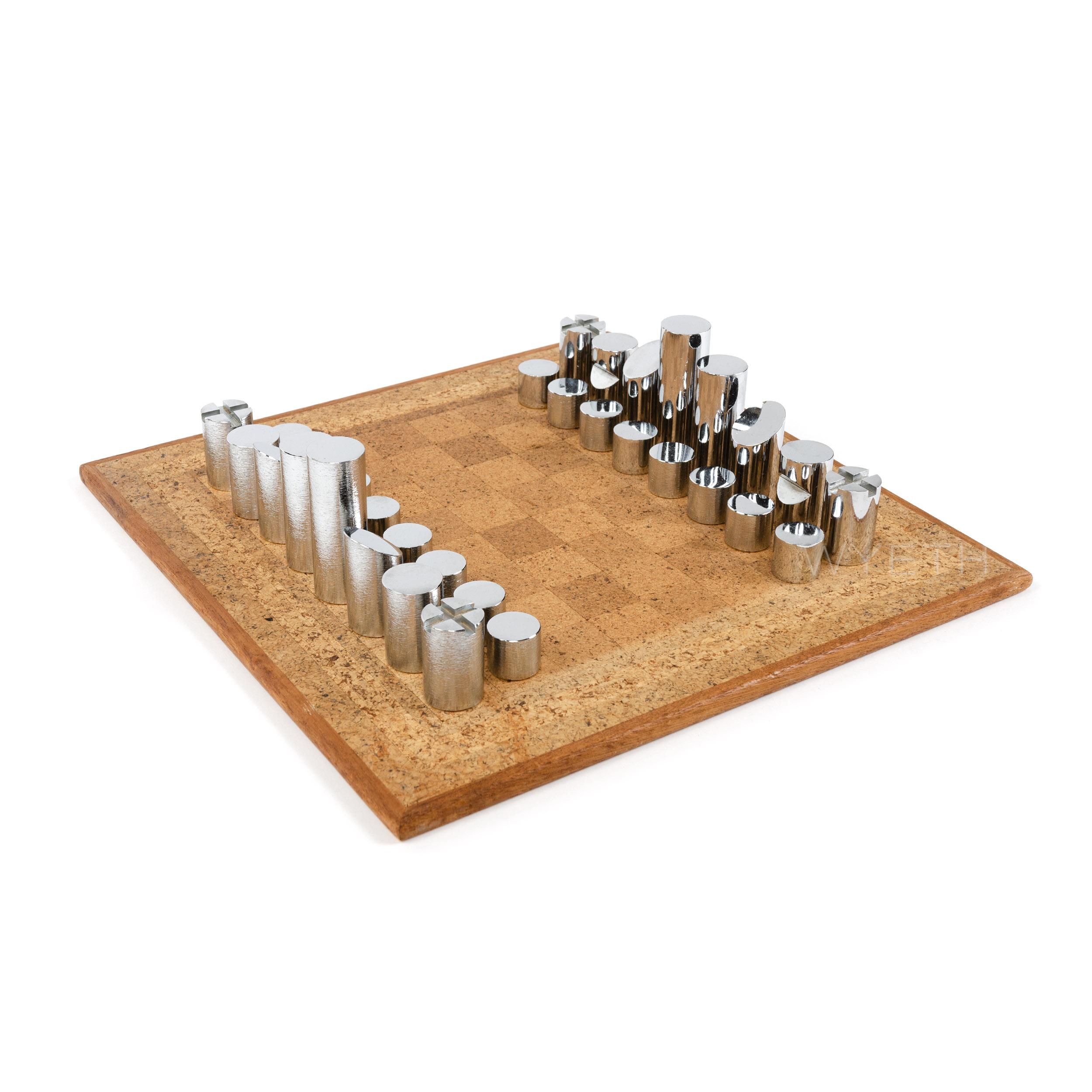 A modernist chess set in chrome-plated brass with a vintage cork board. The pieces are differentiated by having either a smooth polished finish or a subtle ripple texture.