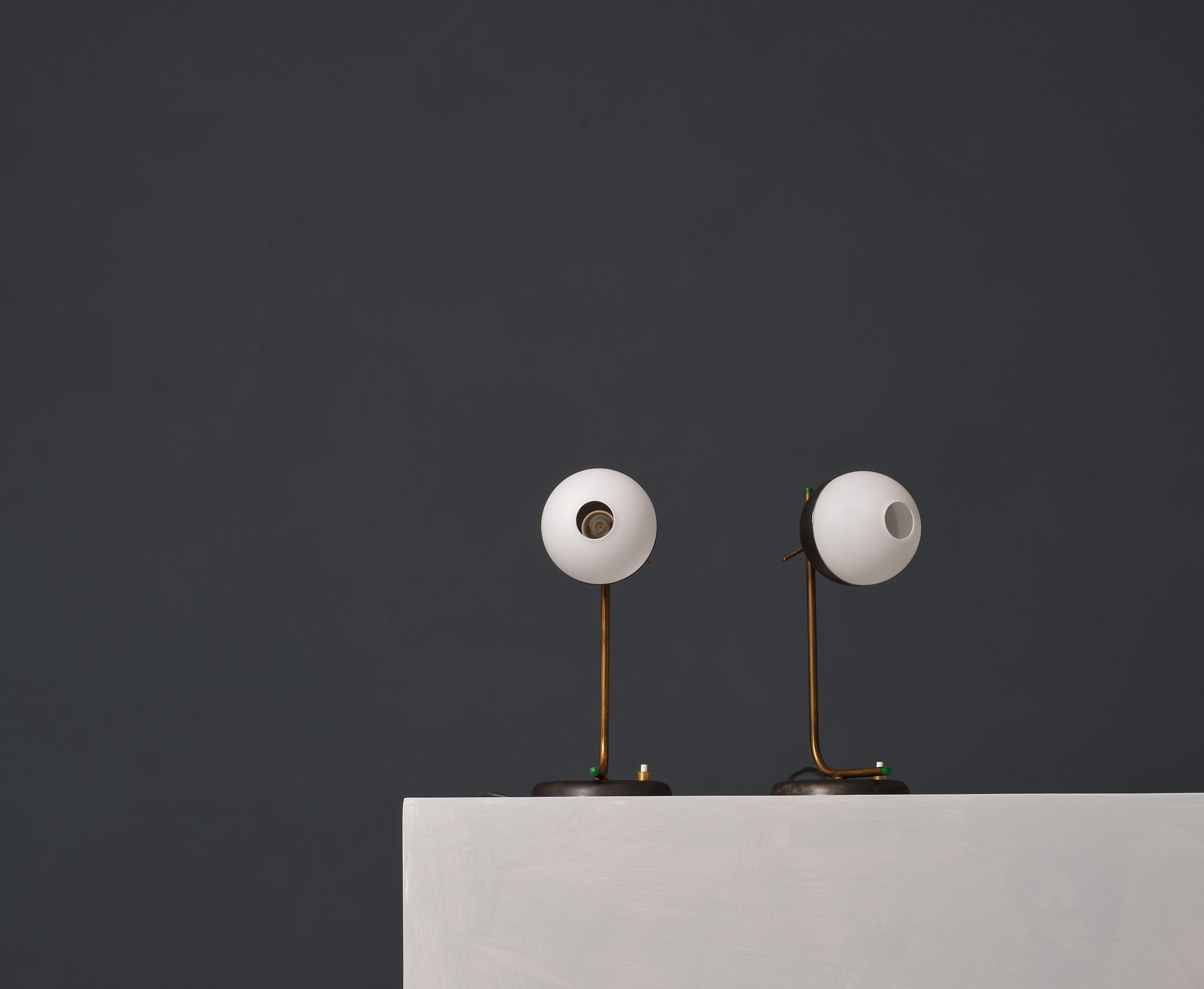 1950s pair of table lamps with modernist design , clean lines and sophisticated material blend. Each lamp features an opaline glass sphere with a distinctive central hole, resembling a monocle, which adds a unique visual interest and allows for a