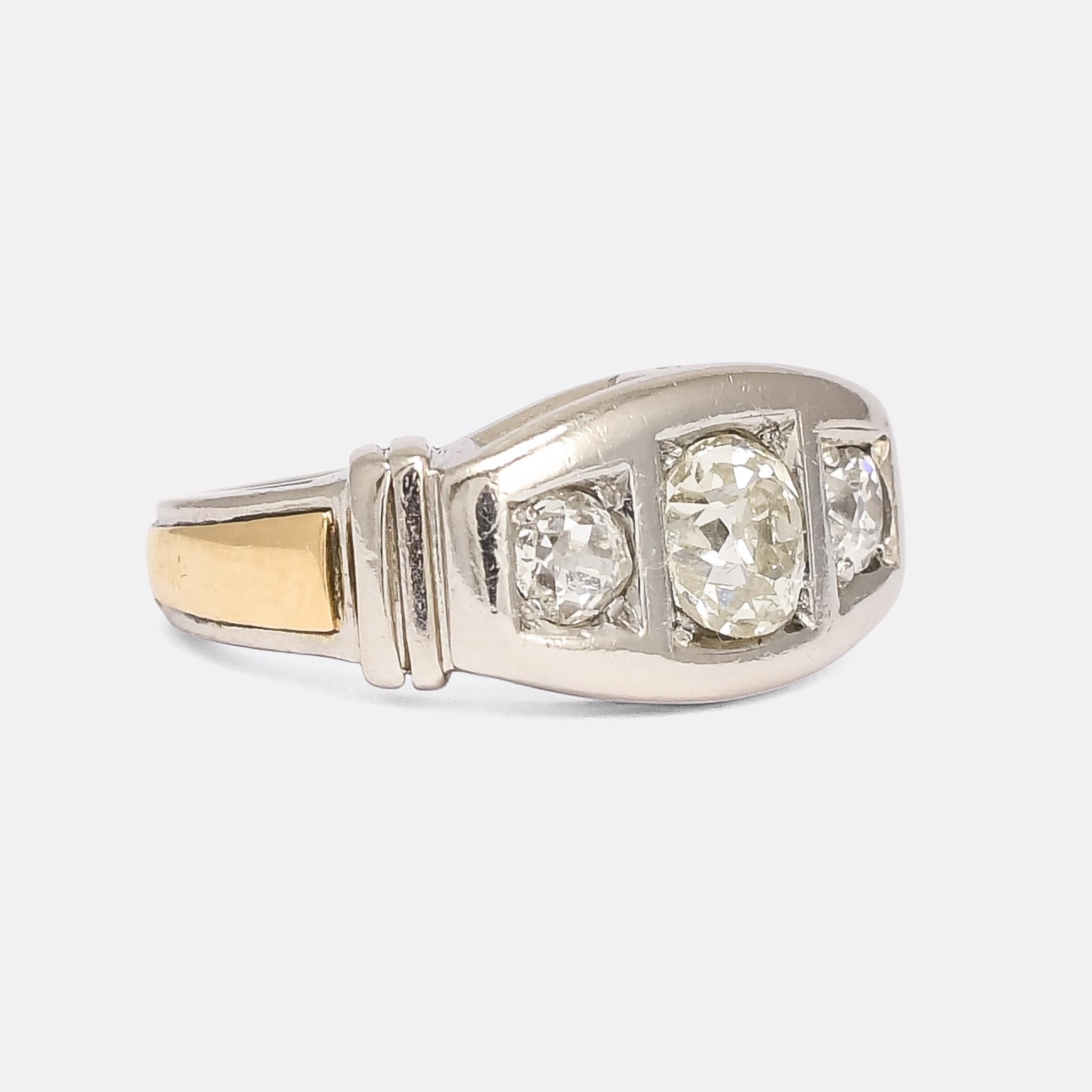 An incredible modernist diamond three-stone ring dating from the 1950s. It's crafted in platinum, with a contrasting 18k gold band around the outer shank, and set with just over 1.30 carats of antique cushion cut diamonds. It's heavy and substantial