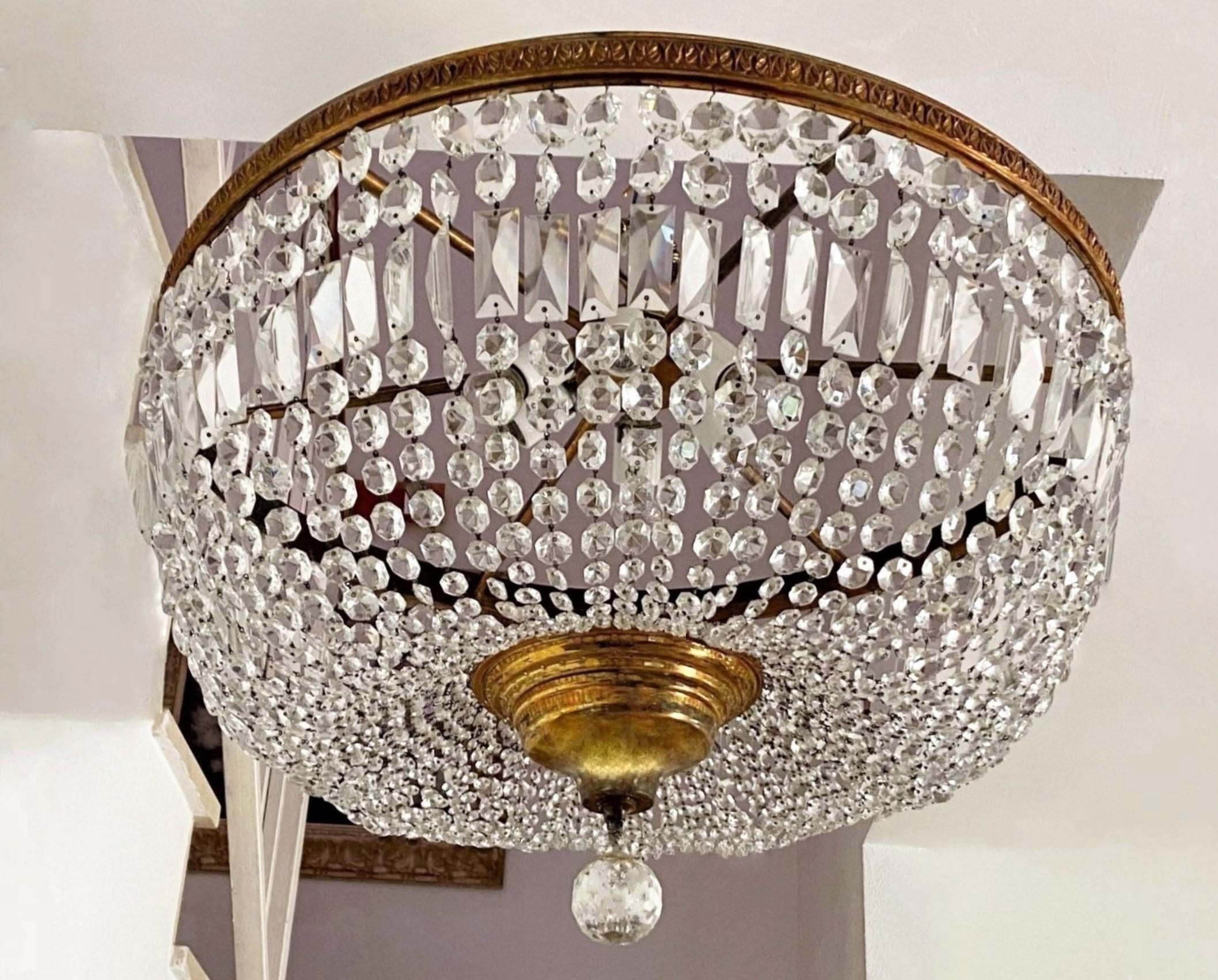 A monumental Art Deco faceted crystal six-light flush mount, France, 1950s. Chains of faceted crystal prismas in several sizes conneting to a solid gilt bronze frame forming a dome ending at the bottom with a large crystal ball. It takes six large