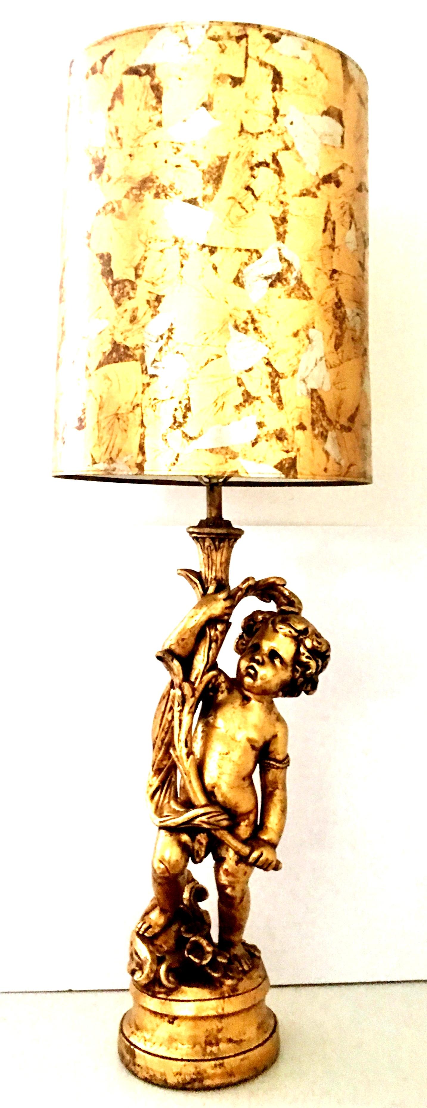 20th Century neoclassical style monumental ceramic gold gilt and gilt brass table lamp with gilt shade. This dramatic Cherub Putti lamp has been executed with incredible attention to detail and features a leaning cherub putti with a floral and fauna