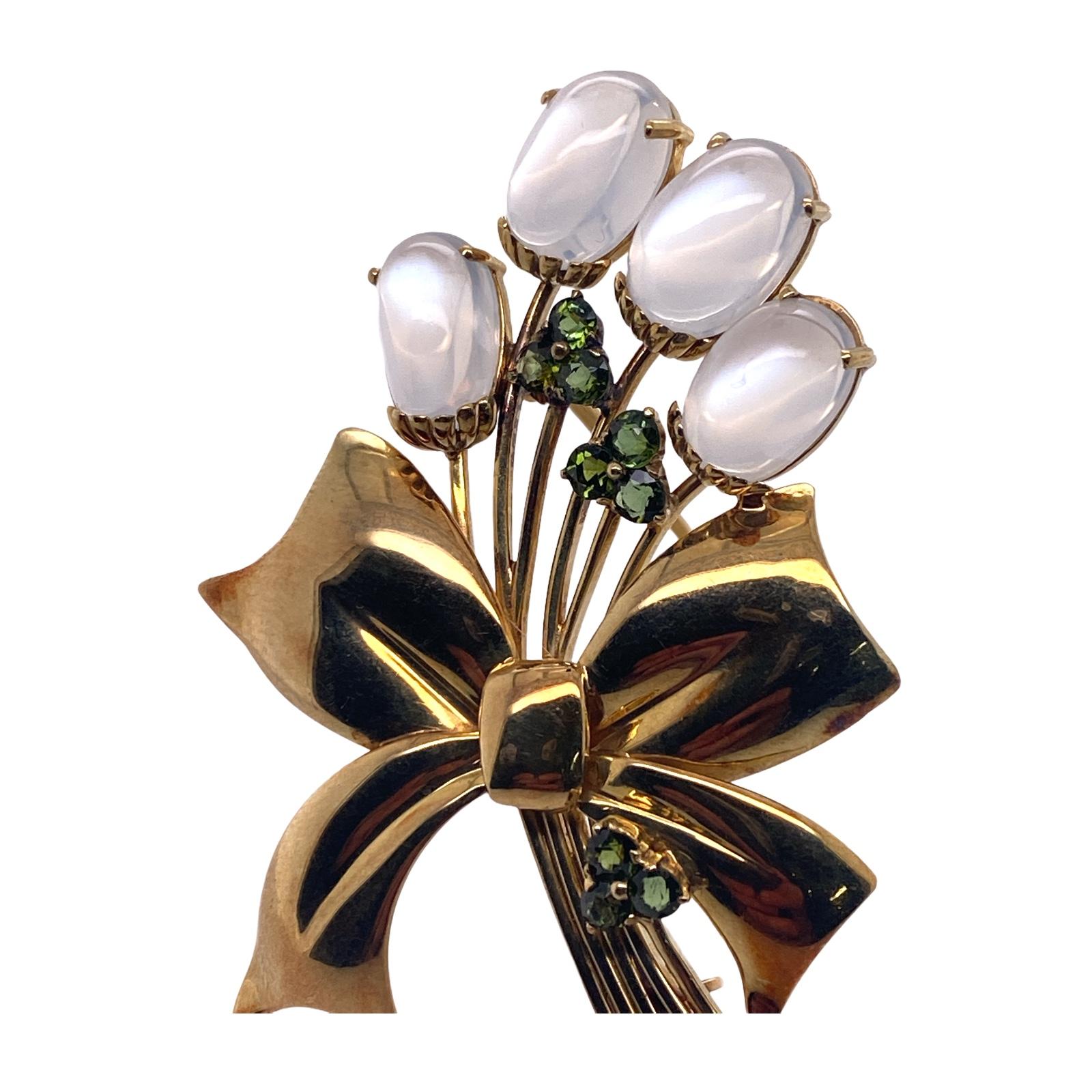 Moonstone and peridot ribbon pin fashioned in 14 Karat yellow gold. The Retro brooch features oval cabochon carved moonstone and round peridot in a wheat ribbon design. The pin measures 40 x 55mm. 