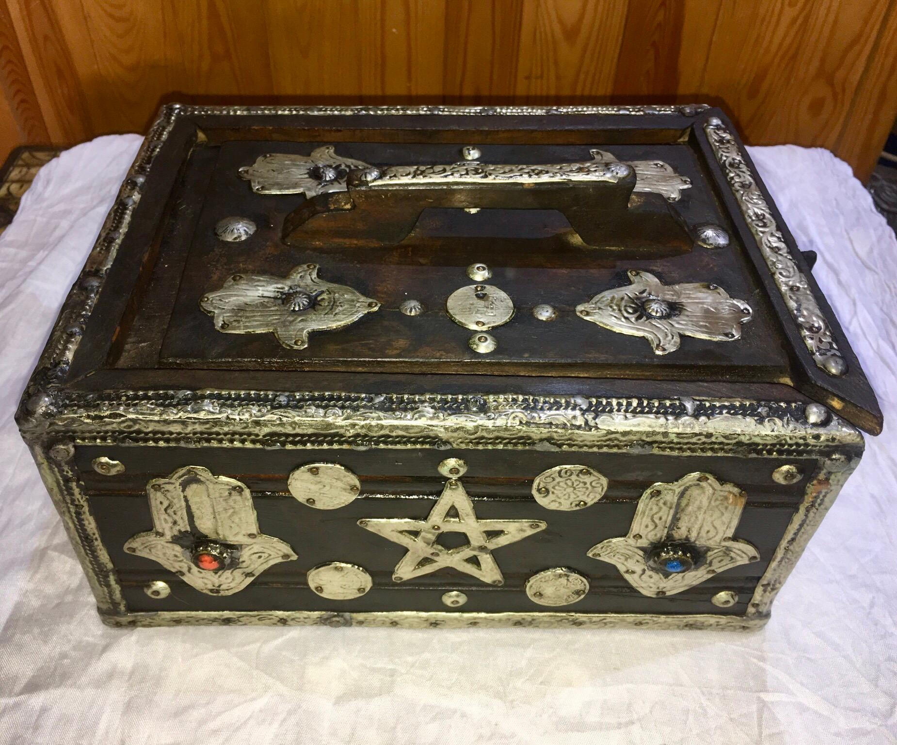 This eye-catching ebony tamarix storage box was once used to store and transport eggs. Made in southern Morocco, the wood is sturdy ebony-colored tamarix with silver and brass repousse, vintage coins, camel bone, and gemstone adornments. 

The front